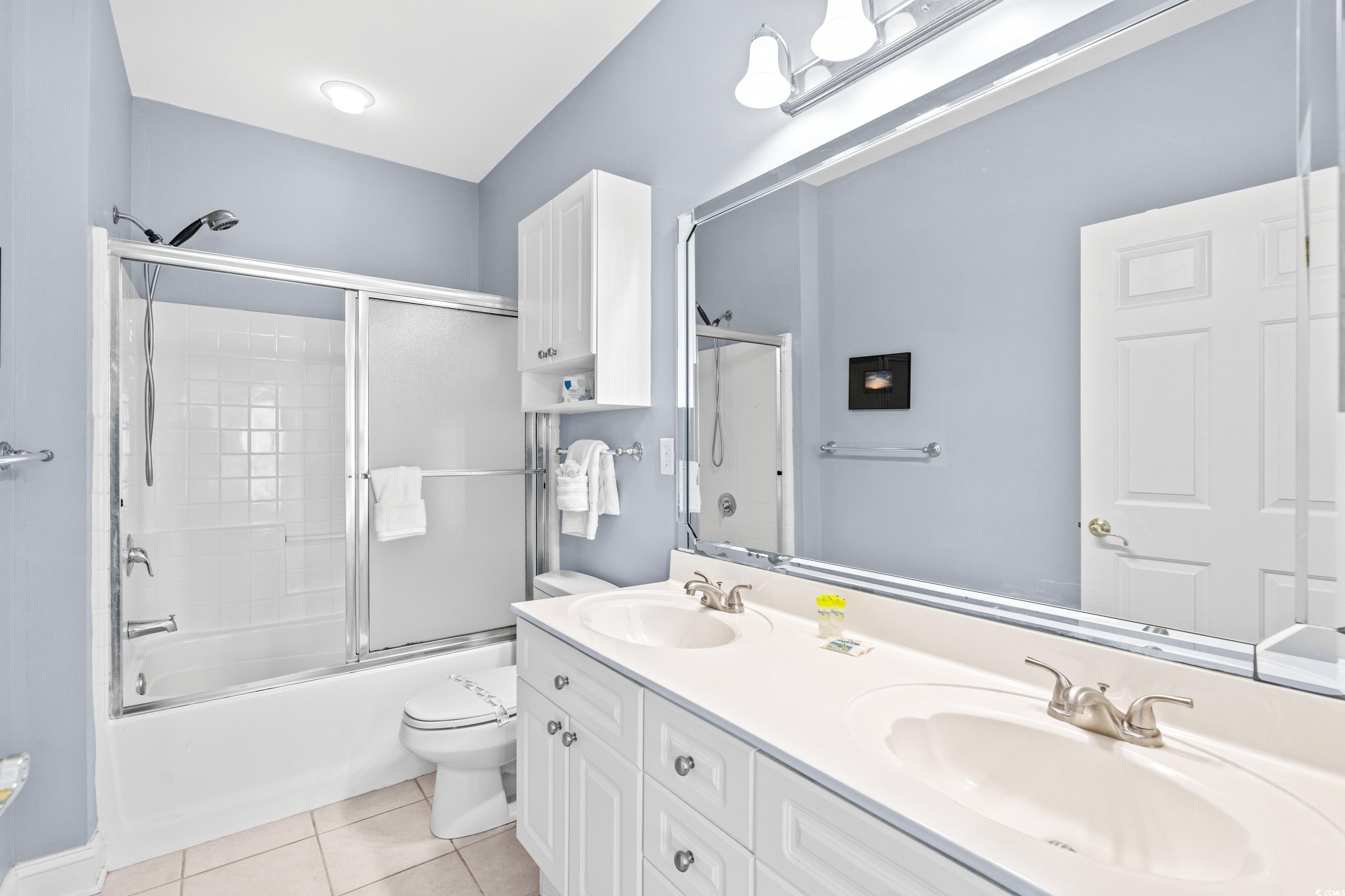 Bathroom with a double-sink vanity and a white tub-shower with sliding glass doors.