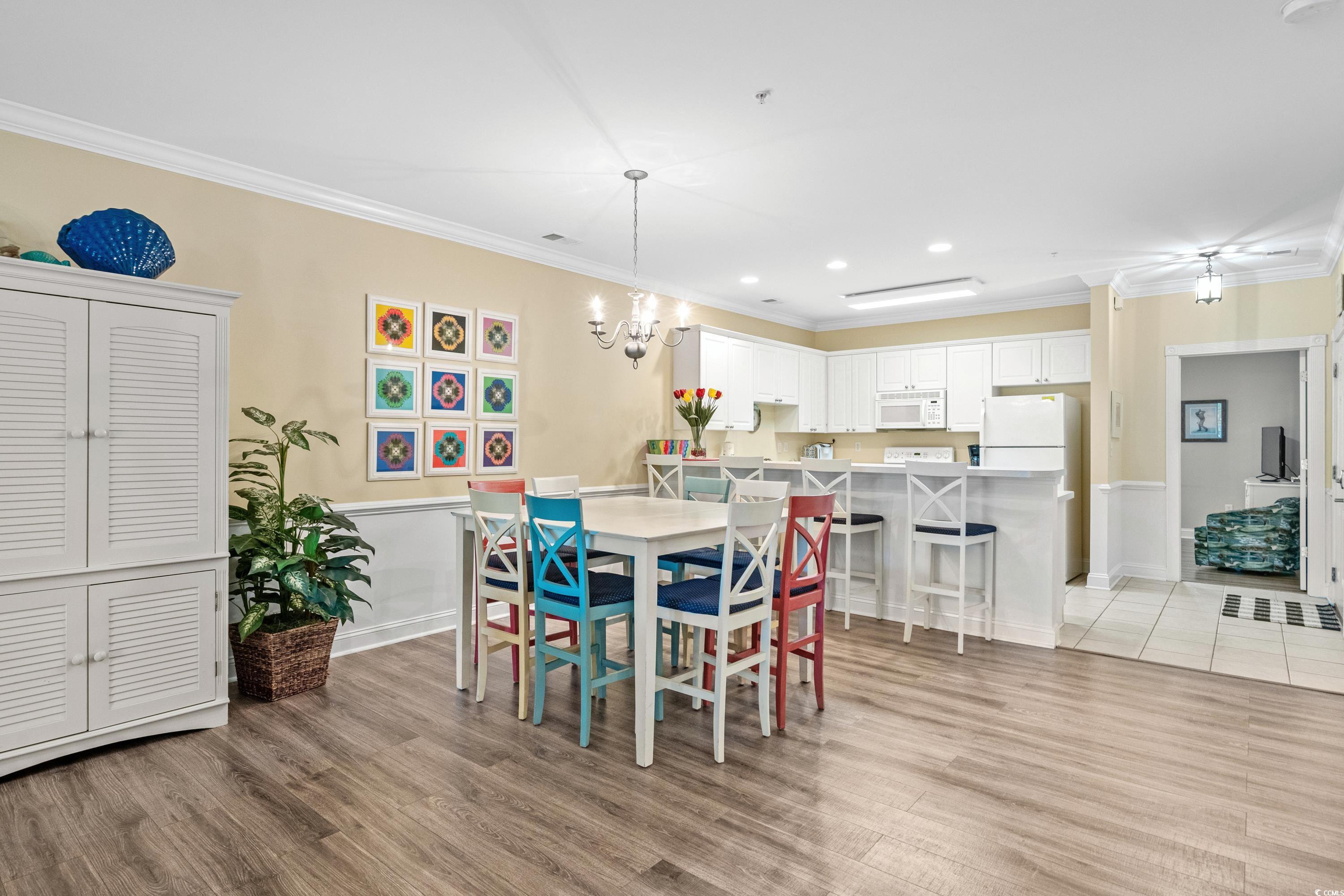 Dining area with colorful chairs beside a white-cabinet kitchen and breakfast bar.