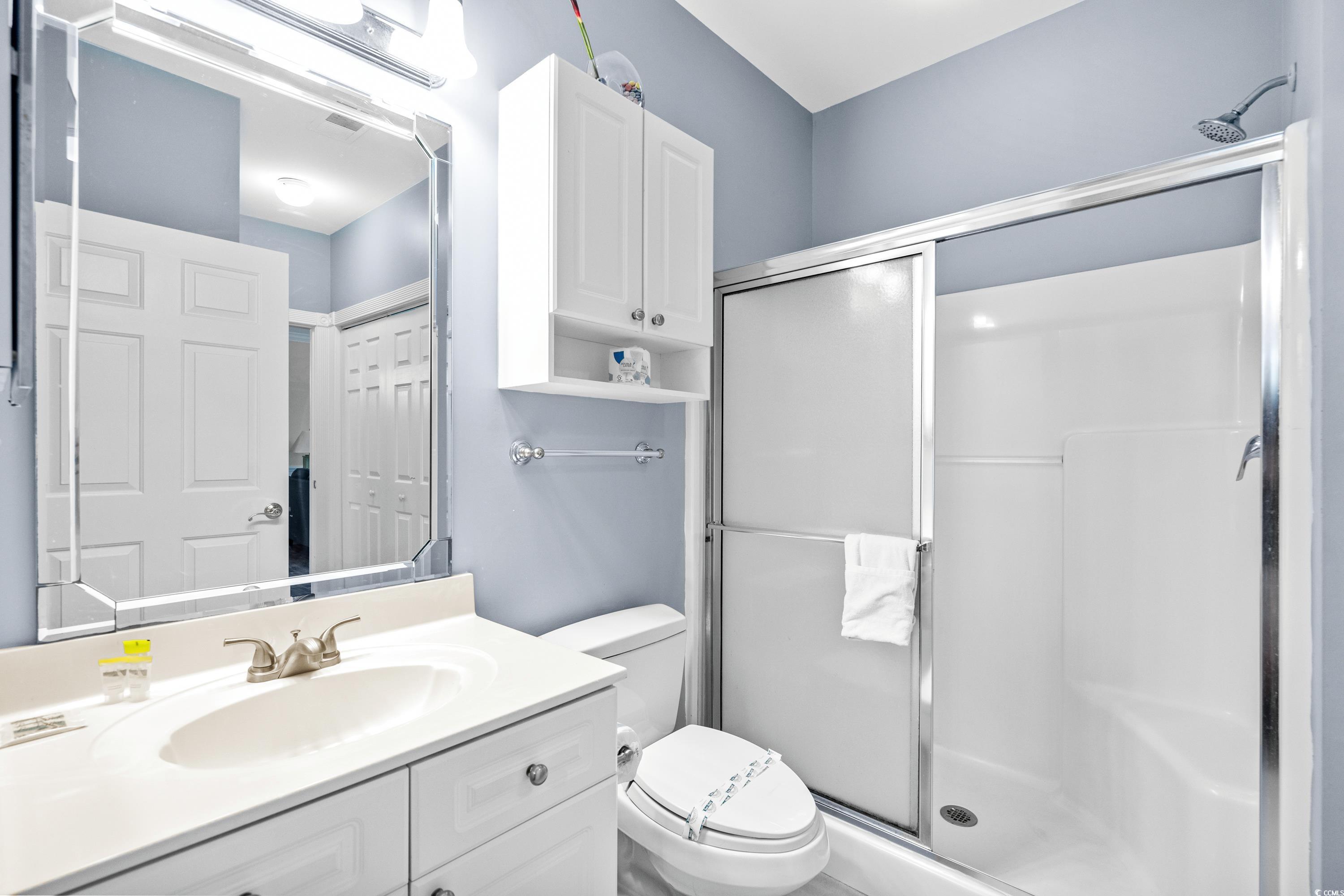 Bathroom with white vanity, large mirror, toilet, and glass-enclosed shower.