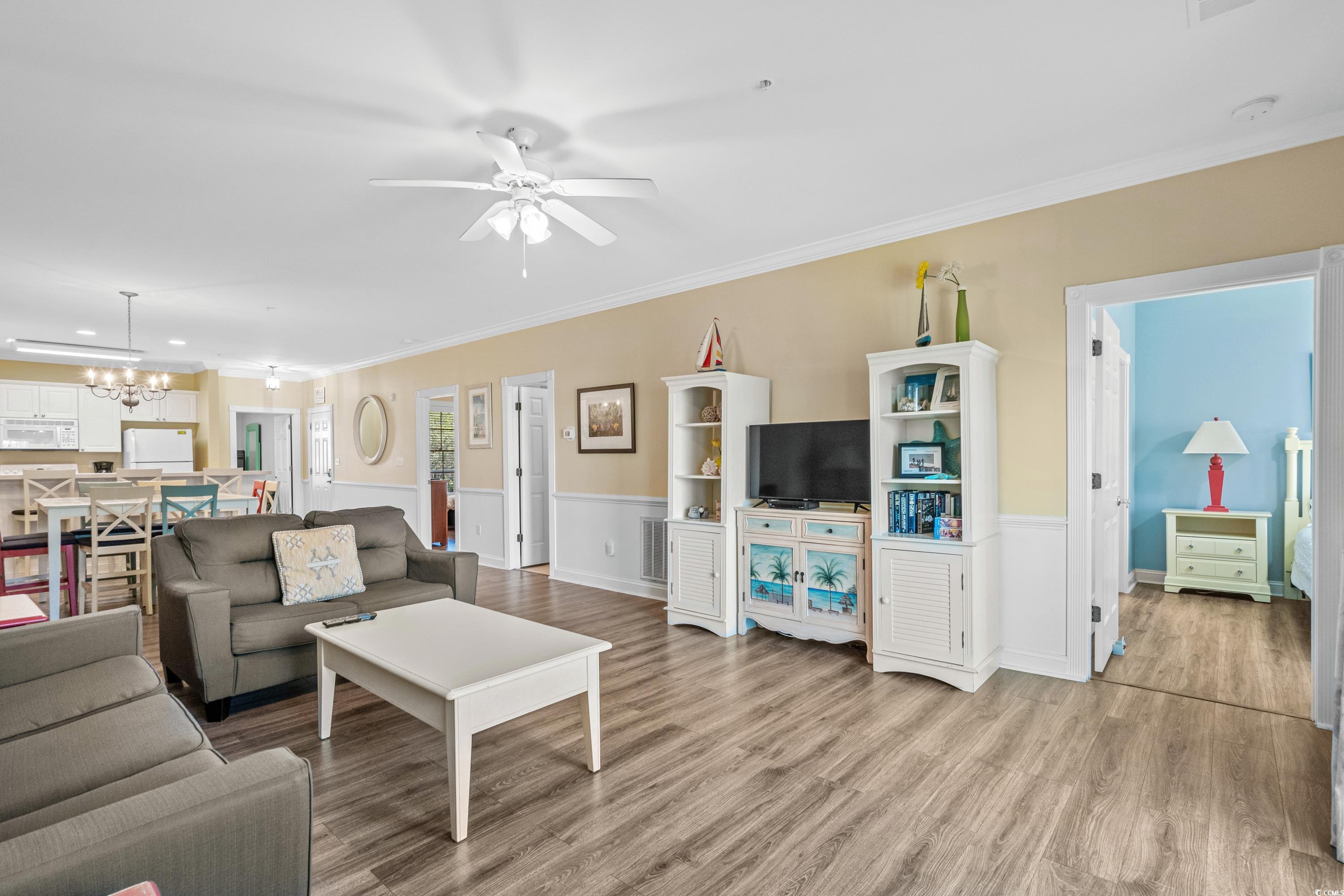 Furnished living room with gray sofas, white TV cabinetry, wood-look floors, and an open doorway to a blue bedroom.