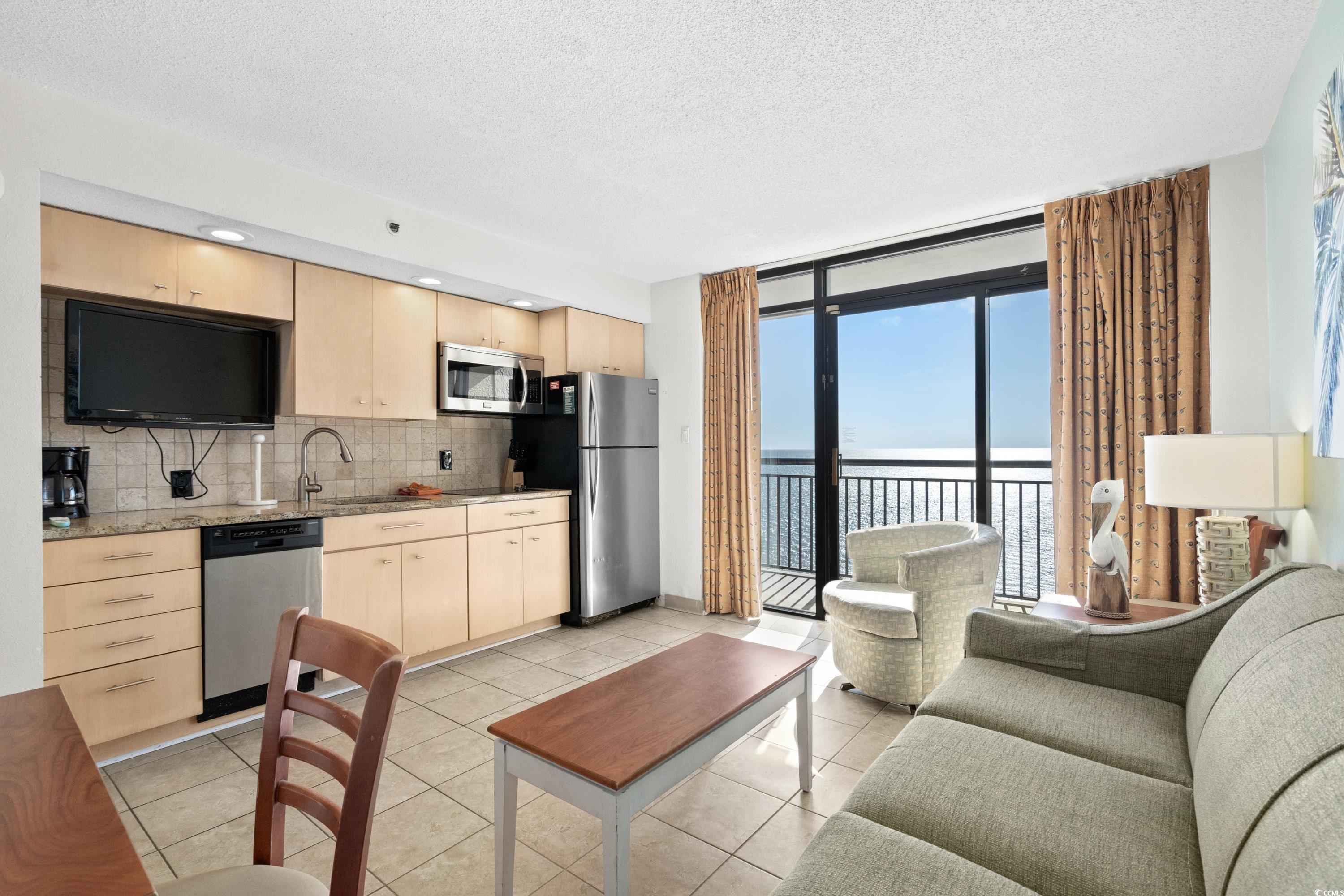 Condo living room and kitchenette with a furnished balcony overlooking the ocean.