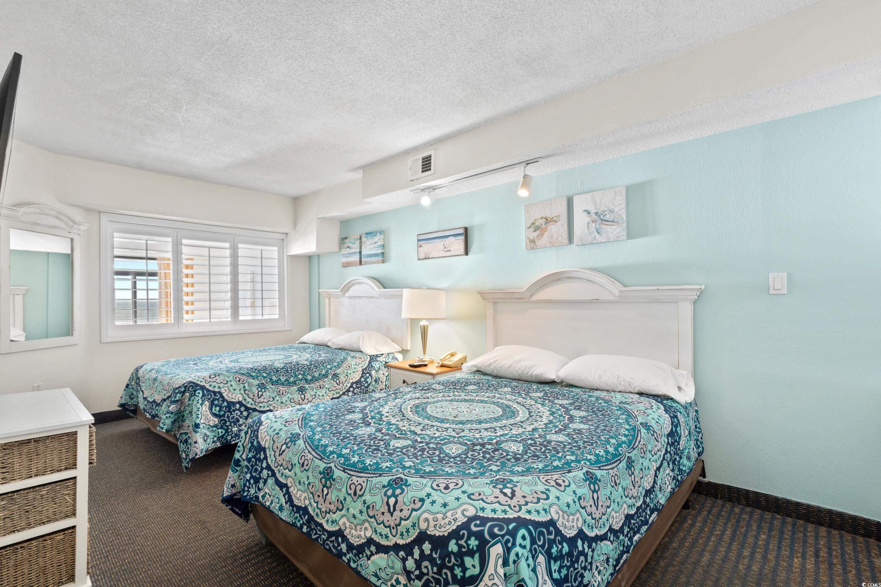 Bedroom with two beds in blue patterned bedding and a pale aqua wall.