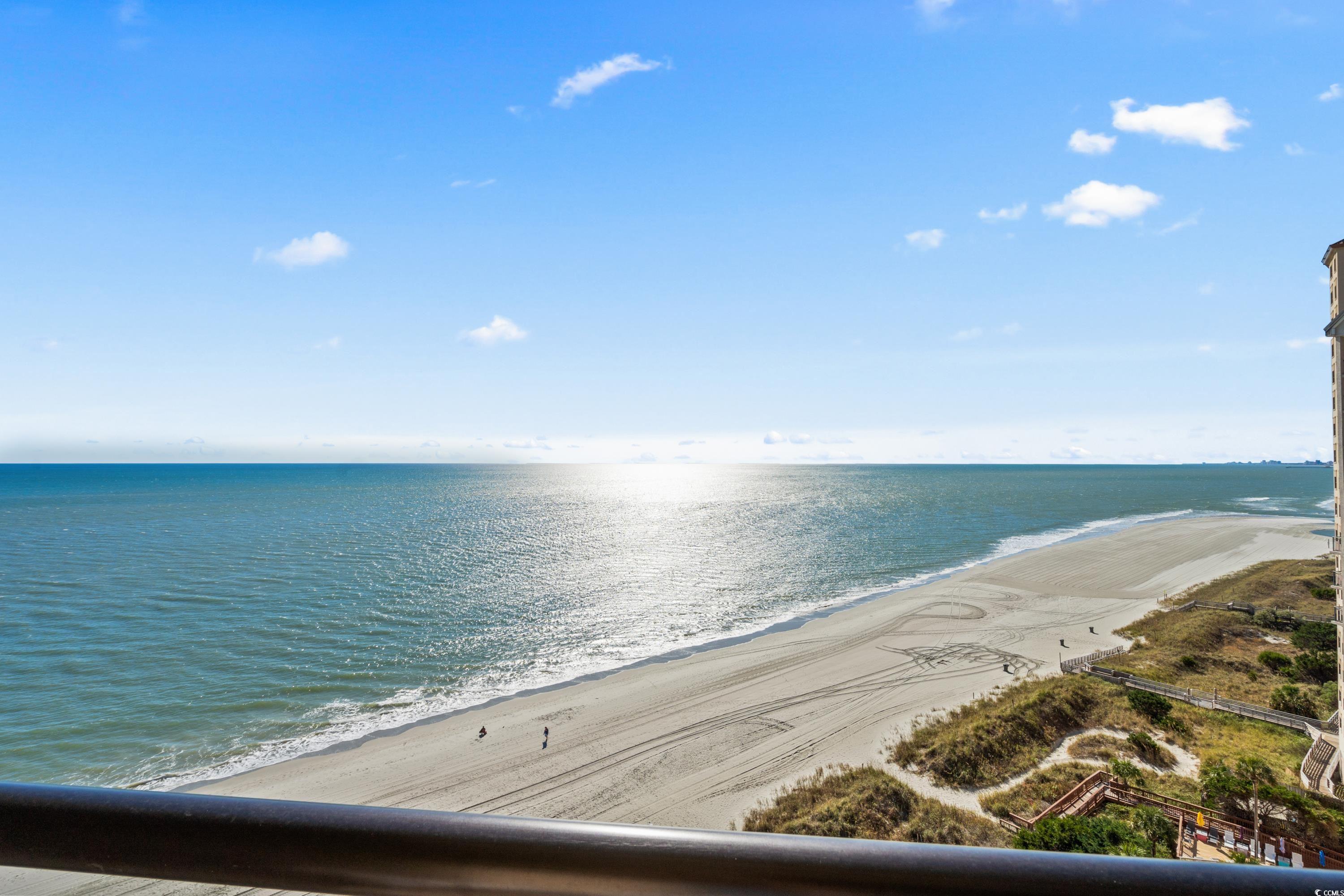 Ocean and sandy beach viewed from a balcony, with sunlight sparkling across the water.