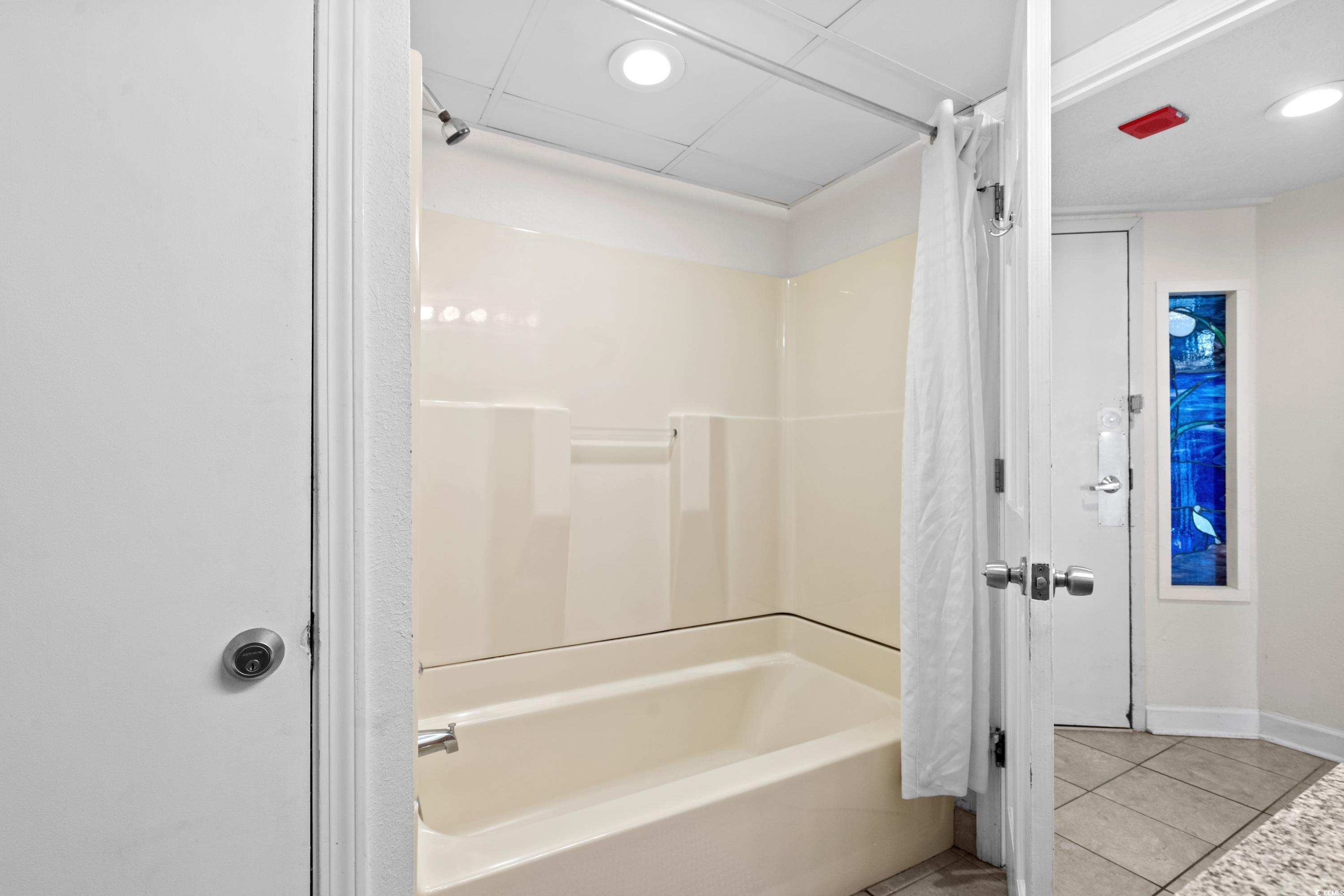 Bathroom with a cream bathtub and shower curtain, viewed from the doorway beside a blue stained-glass panel.