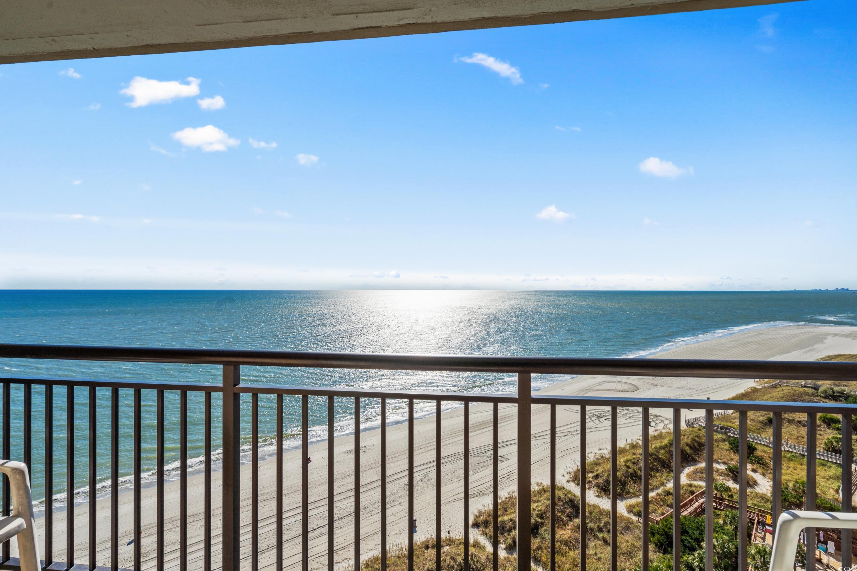 Ocean and sandy beach viewed from a high-rise balcony, with the railing and shoreline in the foreground.