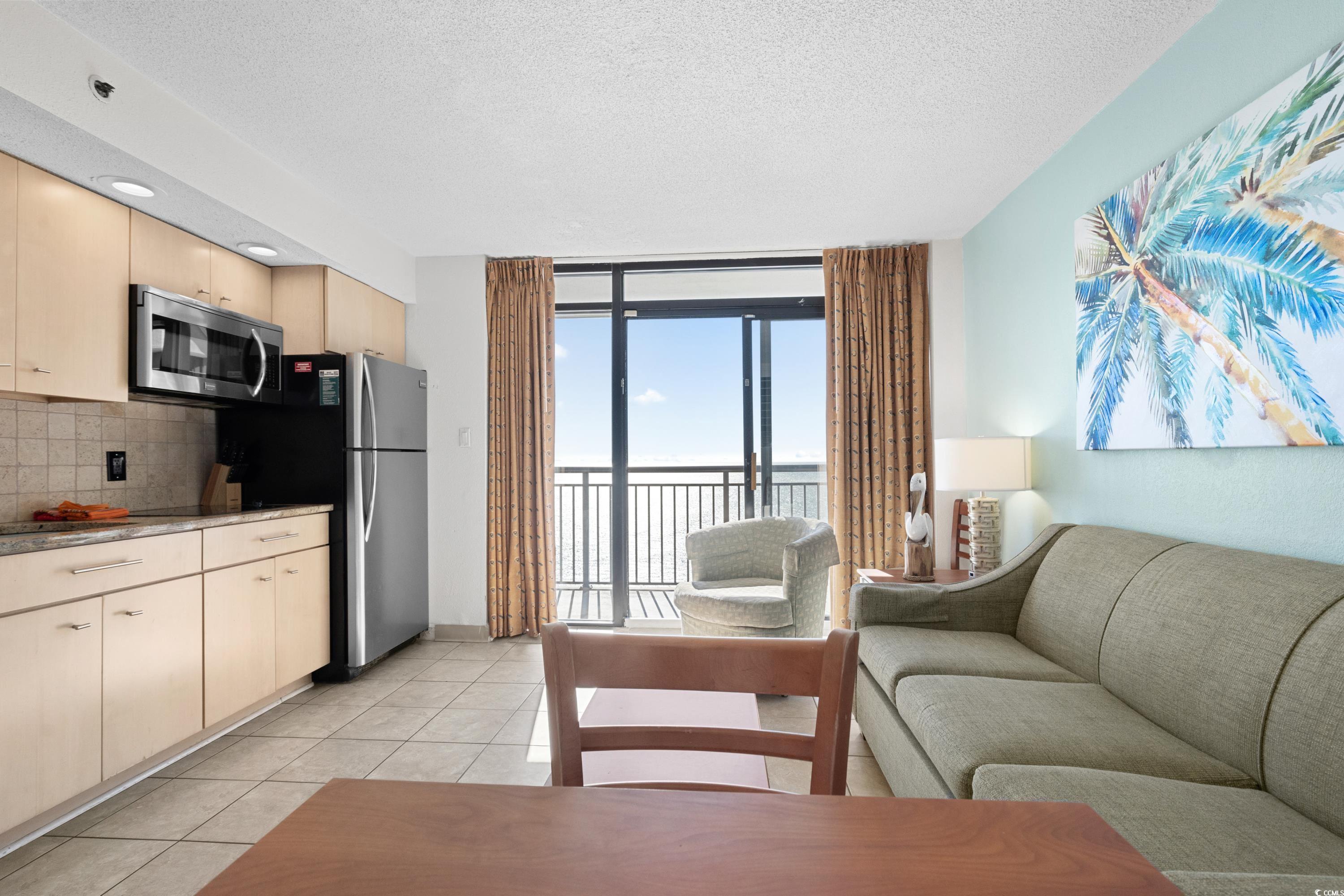 Furnished condo living room and kitchenette with a gray sofa and ocean view from the balcony doors.