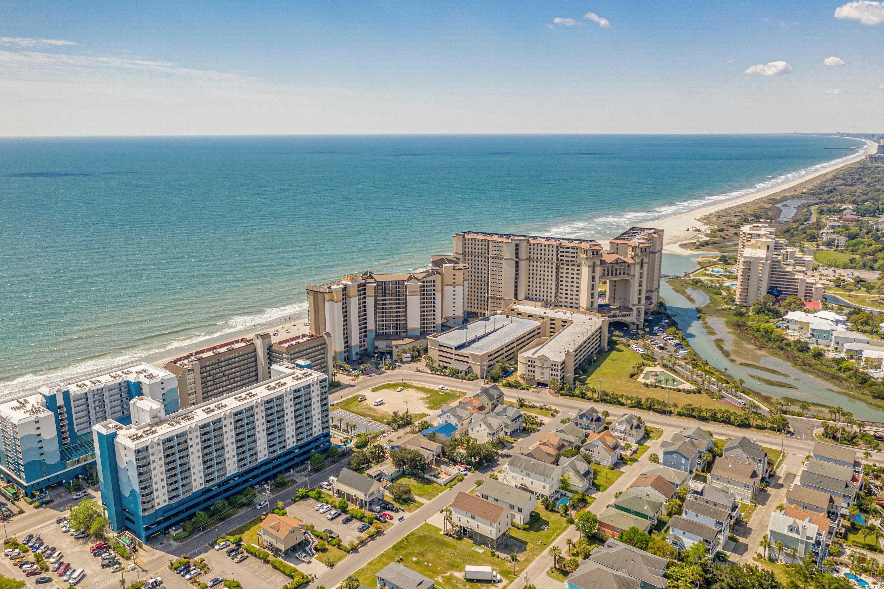 Aerial view of beachfront condominium towers, sandy shoreline, ocean, and nearby homes.