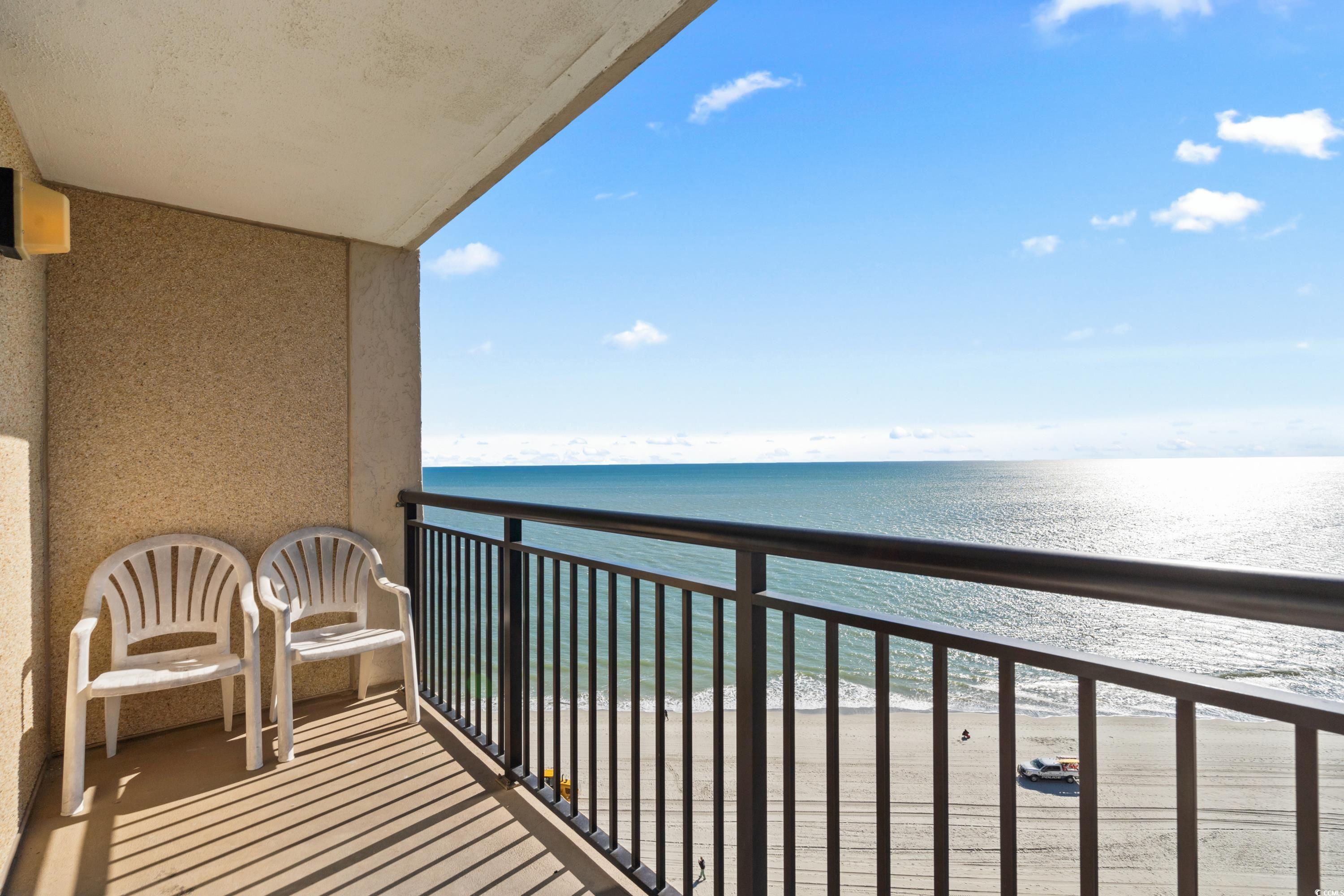Oceanfront balcony with two white chairs overlooking the beach and ocean.
