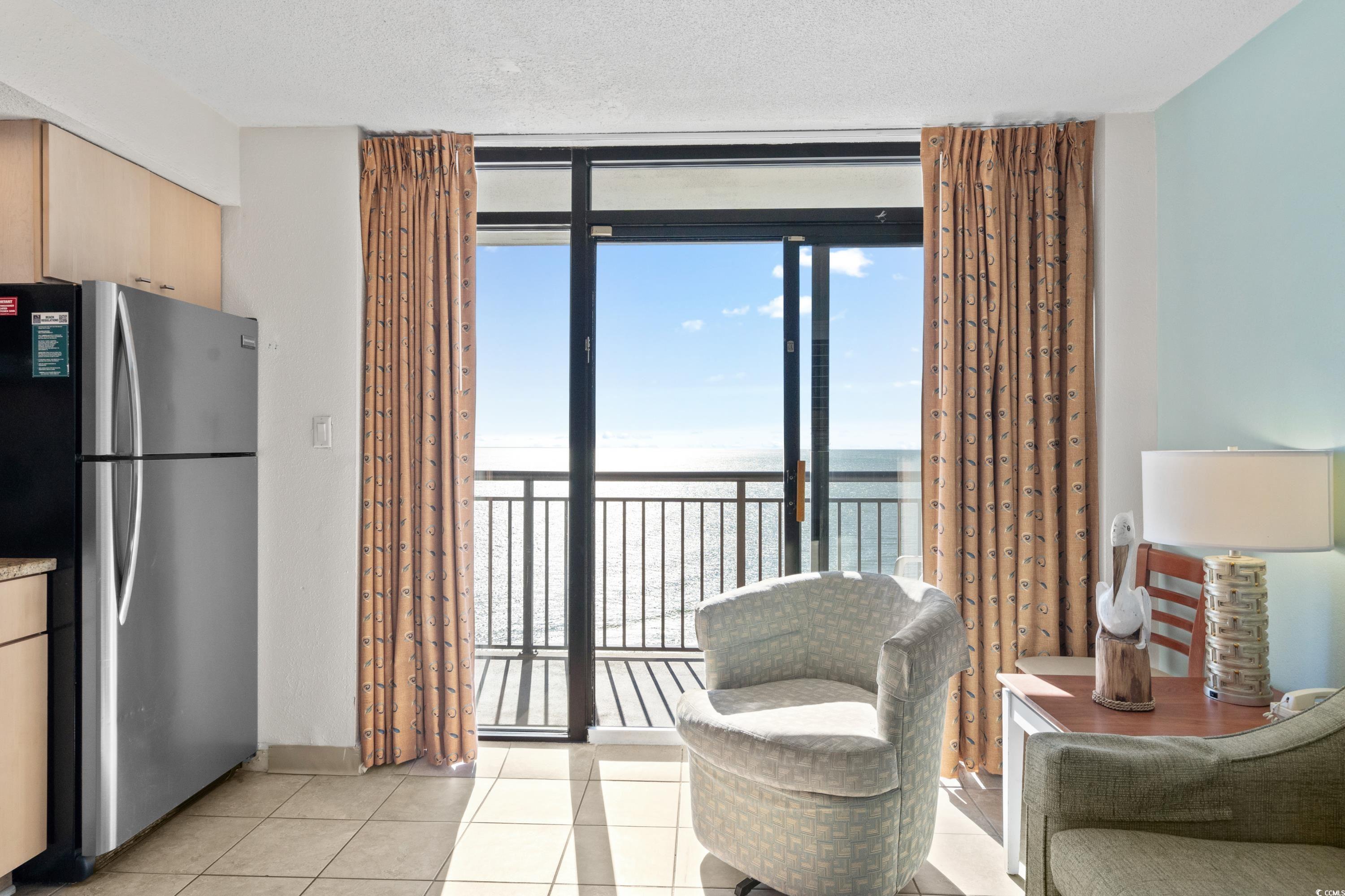 Furnished condo living area with sliding doors to an ocean-view balcony and a kitchenette.