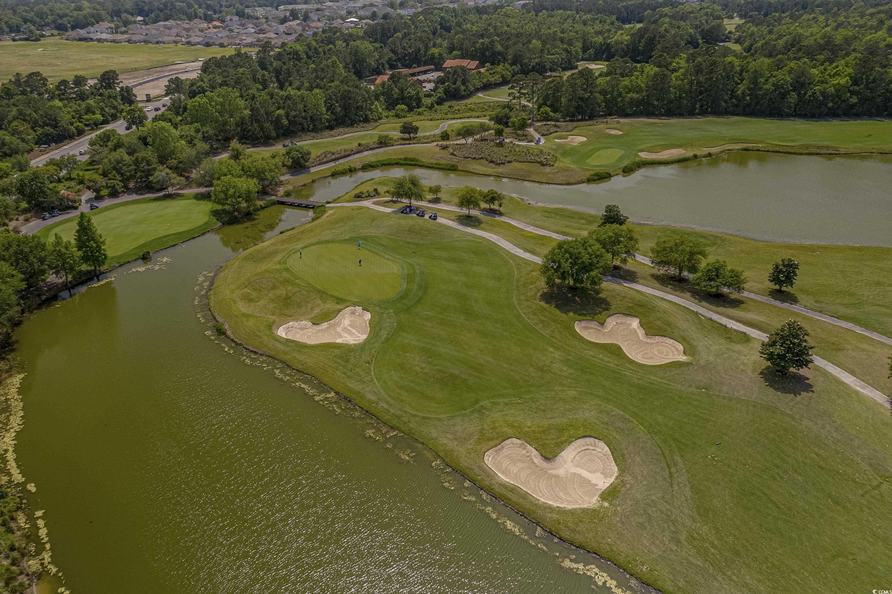 Aerial golf course with sculpted sand bunkers beside ponds and a winding cart path.