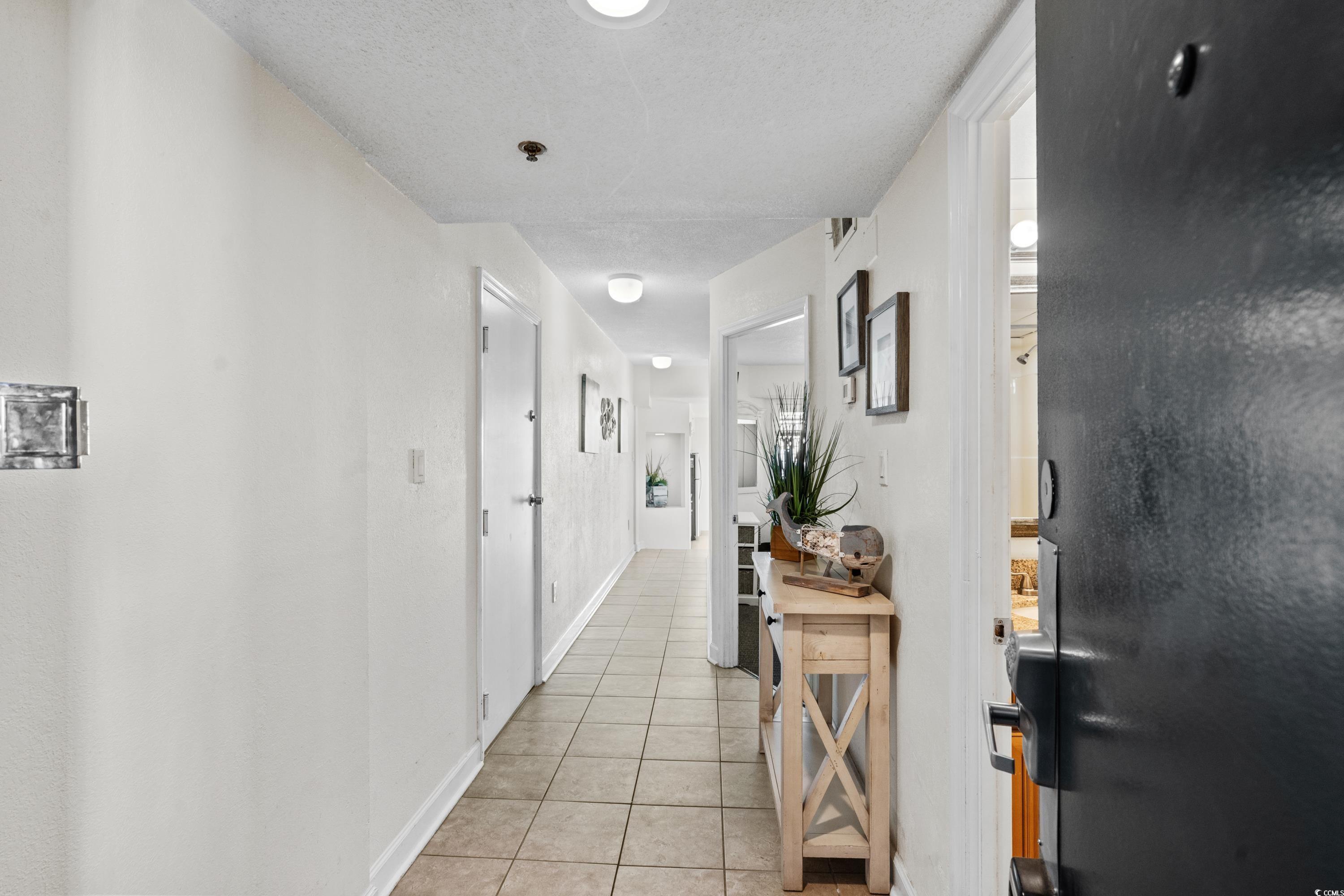 Condominium entry hallway with tiled floors, a wooden console table, and an open dark front door.