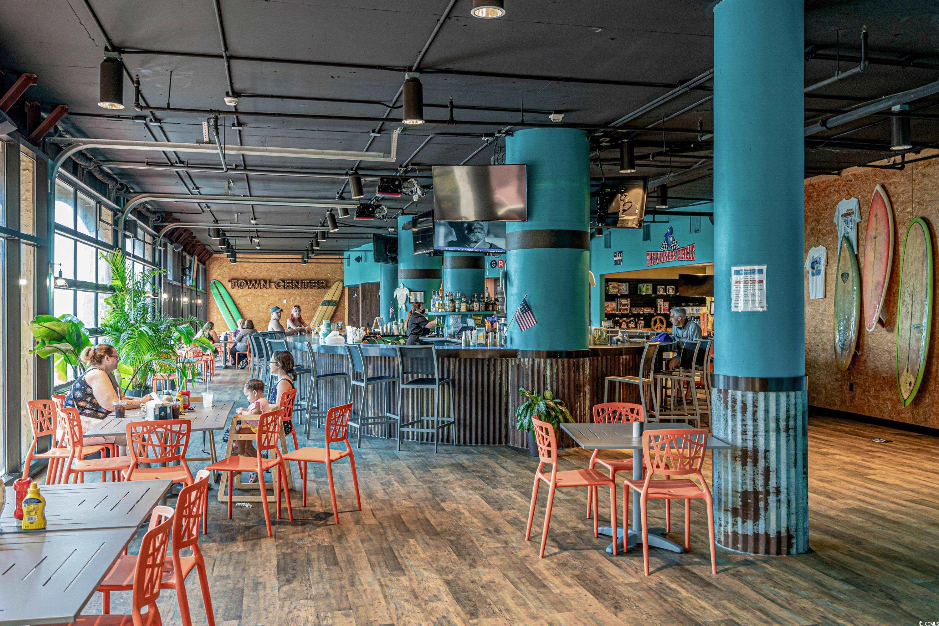 Indoor dining area with a long bar, turquoise columns, coral chairs, and surfboards on the wall.
