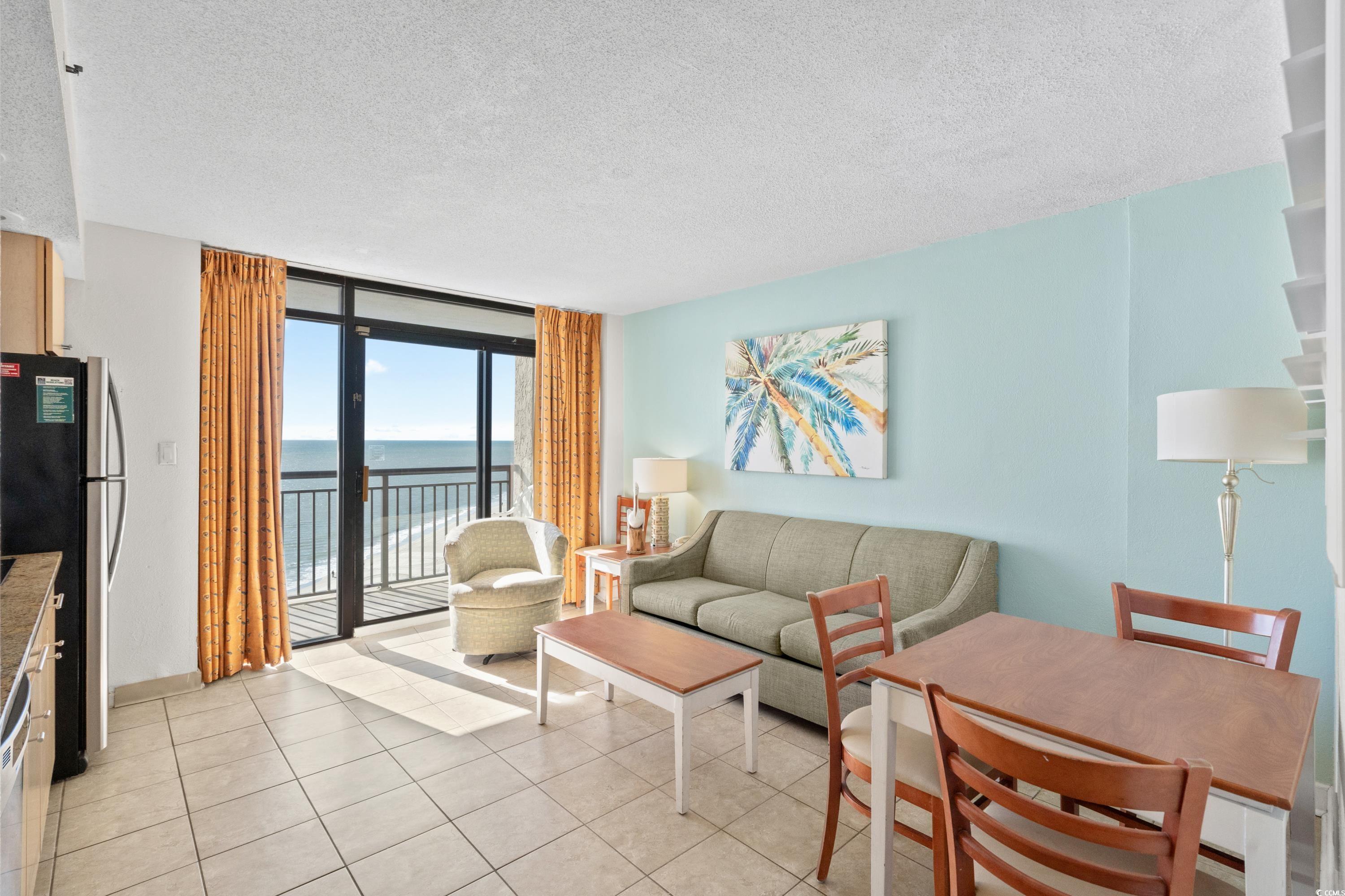 Oceanfront condo living and dining area with a furnished balcony view through sliding glass doors.