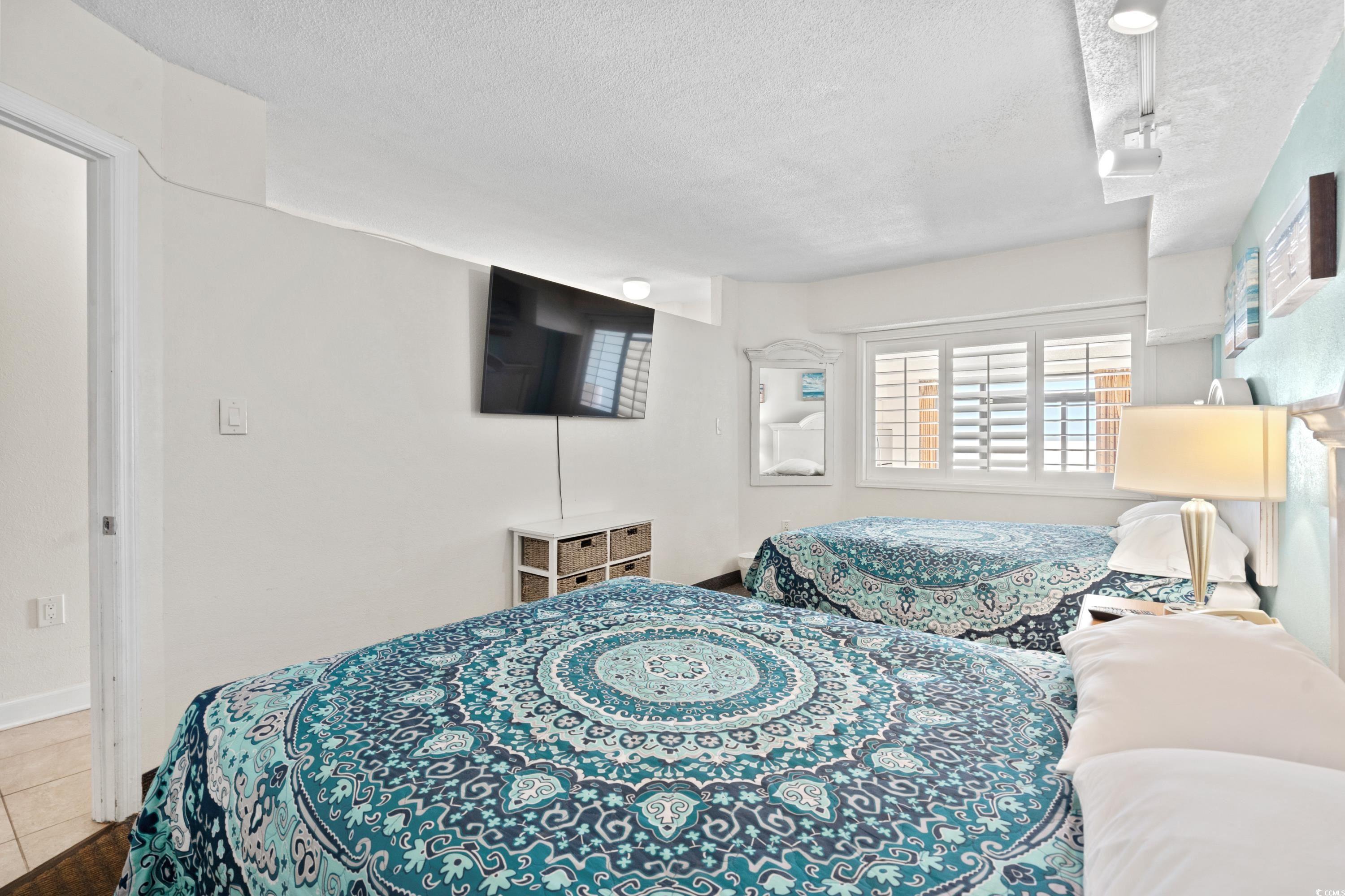 Bedroom with two blue-patterned beds, a wall-mounted television, and a shuttered window.