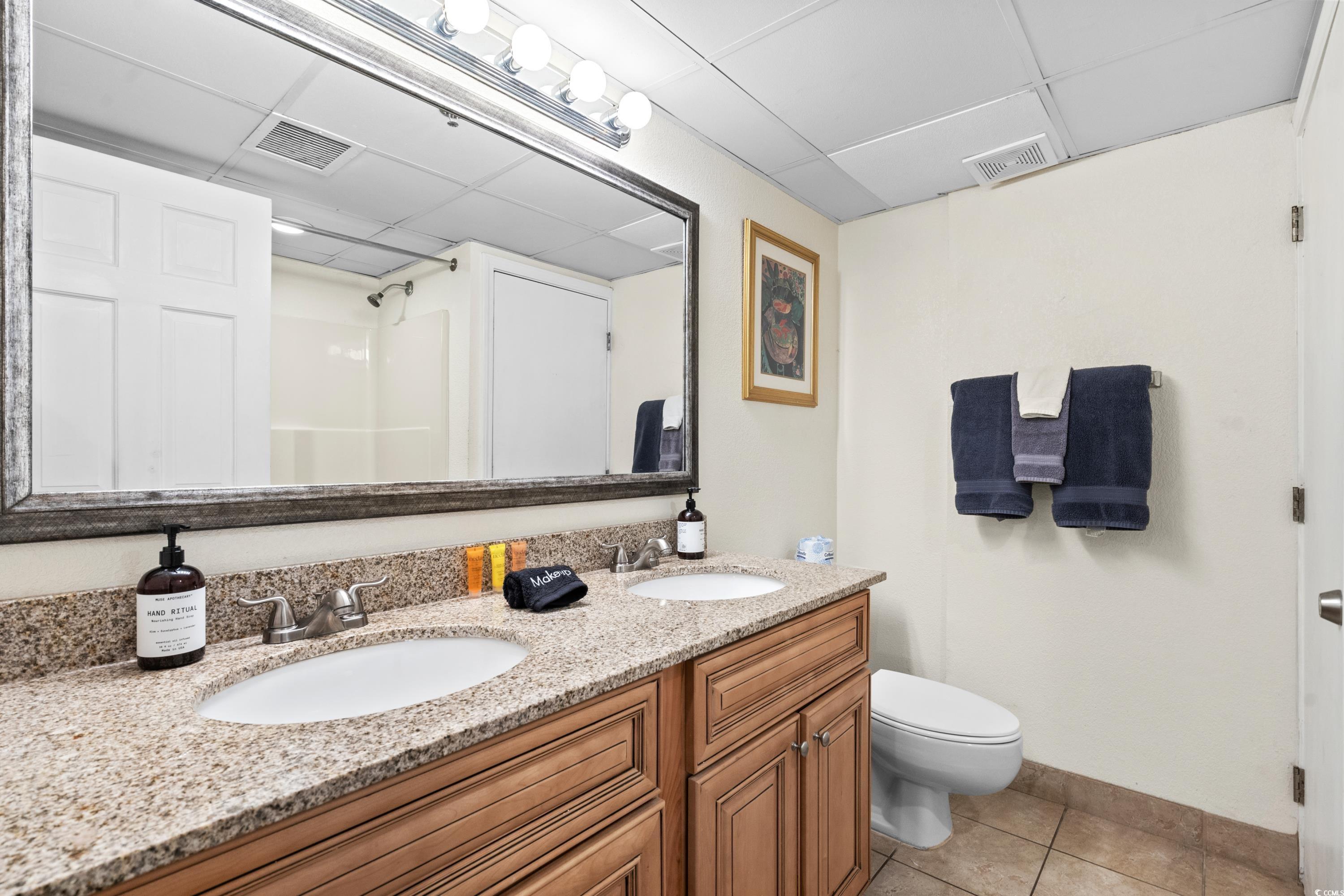 Bathroom with a double-sink granite vanity, wood cabinets, large mirror, and navy towels.