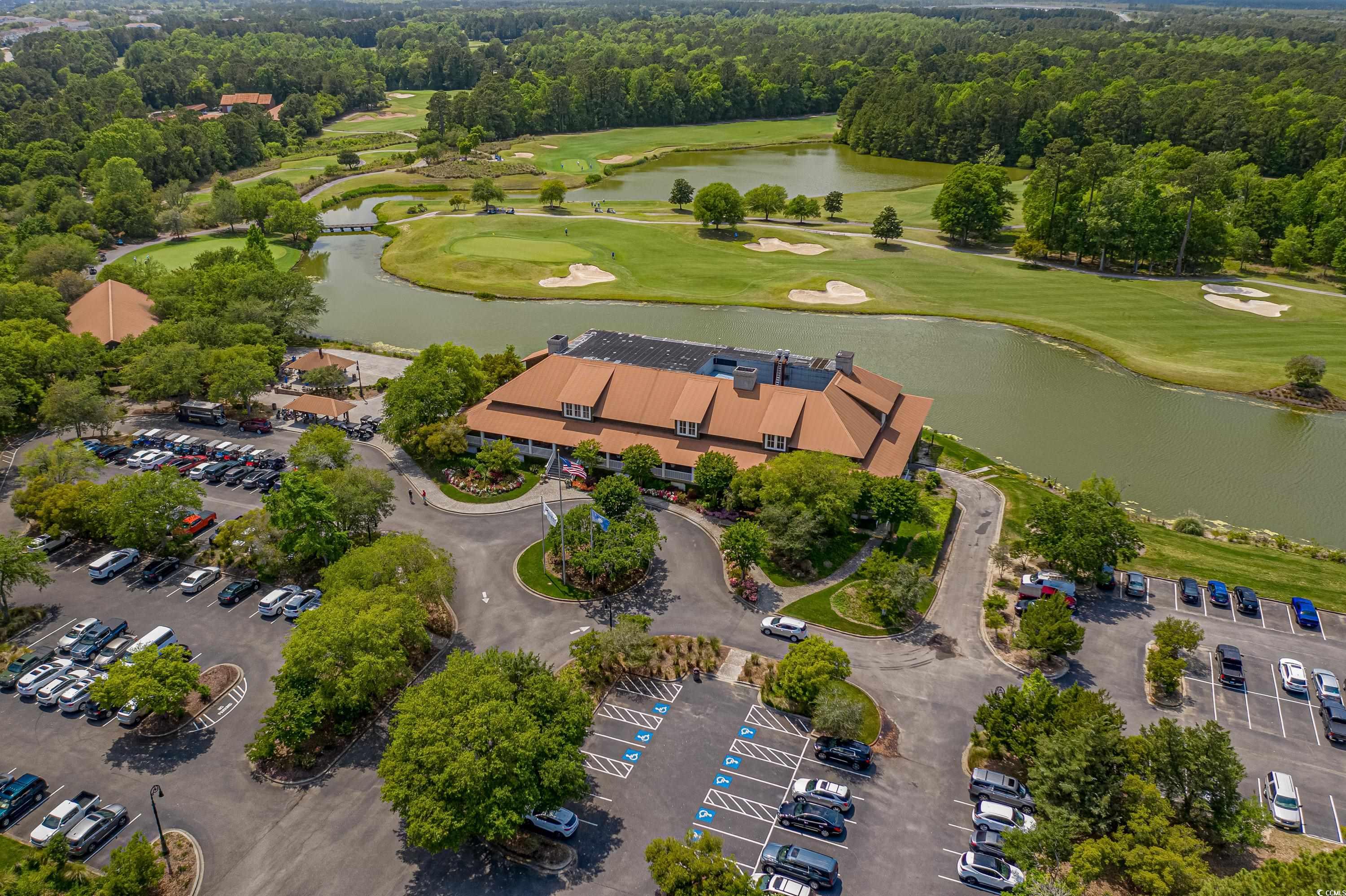 Aerial view of a golf course, clubhouse, ponds, and surrounding parking areas.