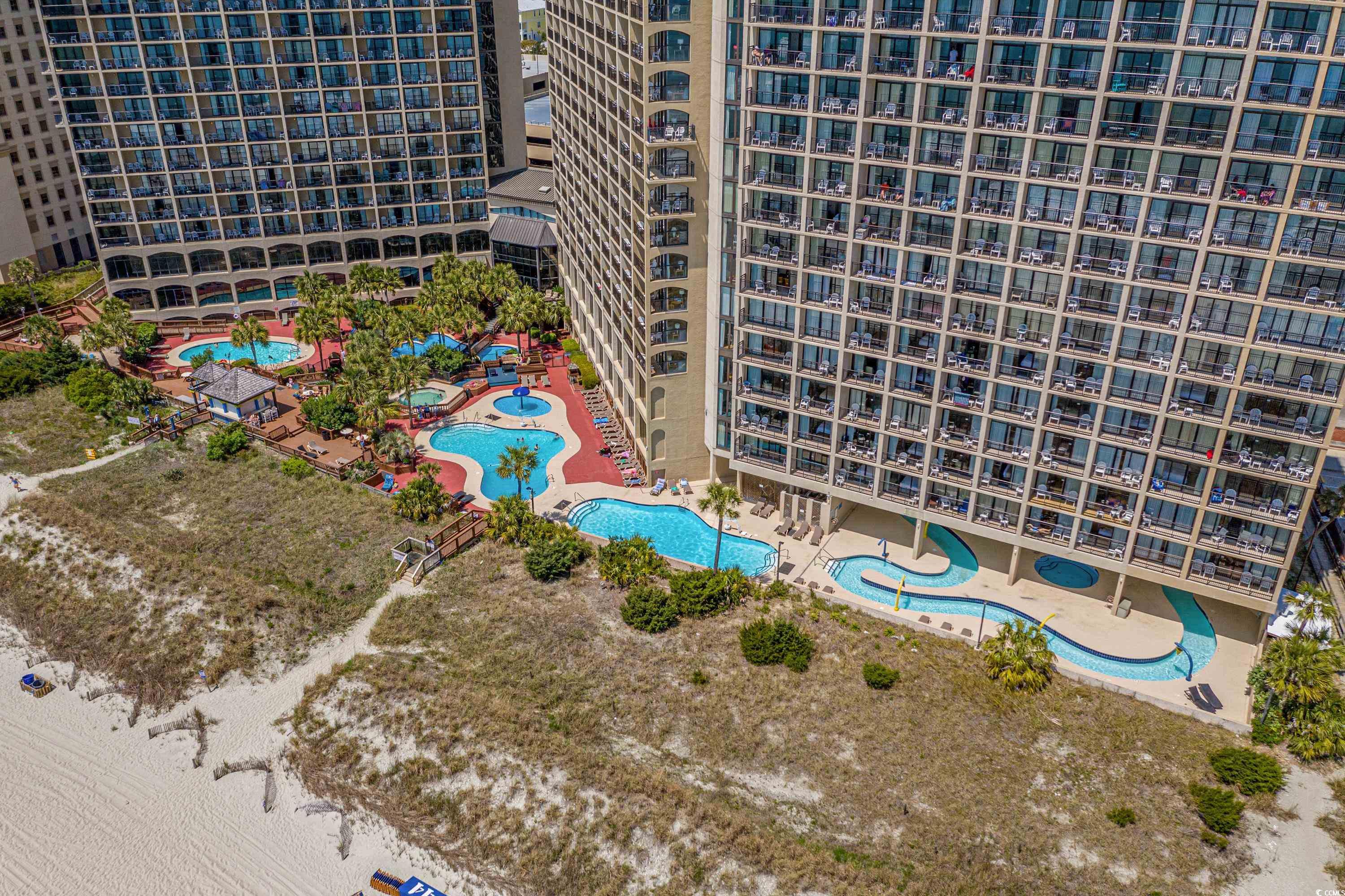 Aerial view of beachfront condominium towers with pools, a lazy river, and sandy beach.