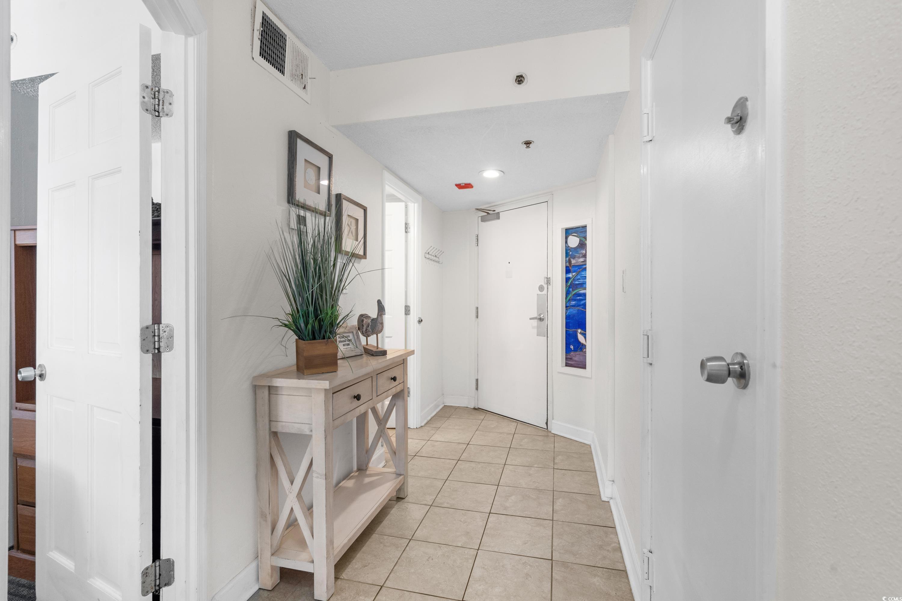Condo entry hallway with beige tile, a white front door, and a console table with a potted plant.