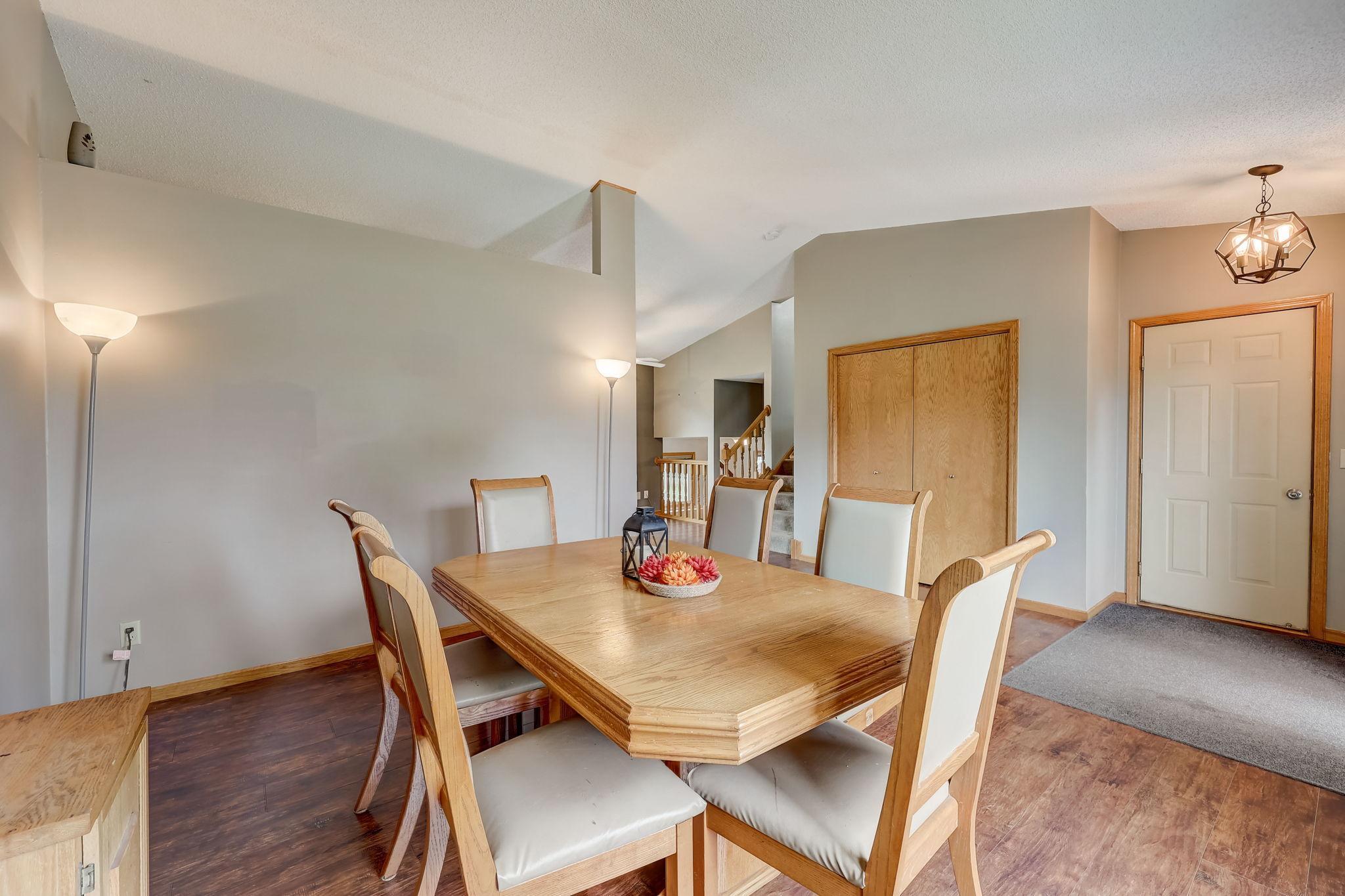 Dining room with a wooden table, upholstered chairs, vaulted ceiling, and nearby entryway.