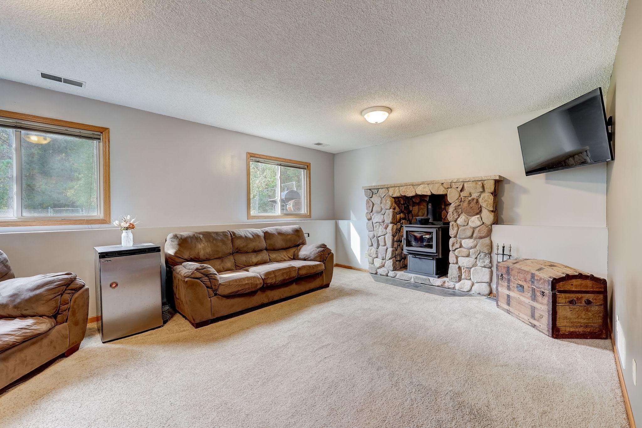 Living room with brown sofas, a stone fireplace and wood-burning stove, and a wall-mounted television.