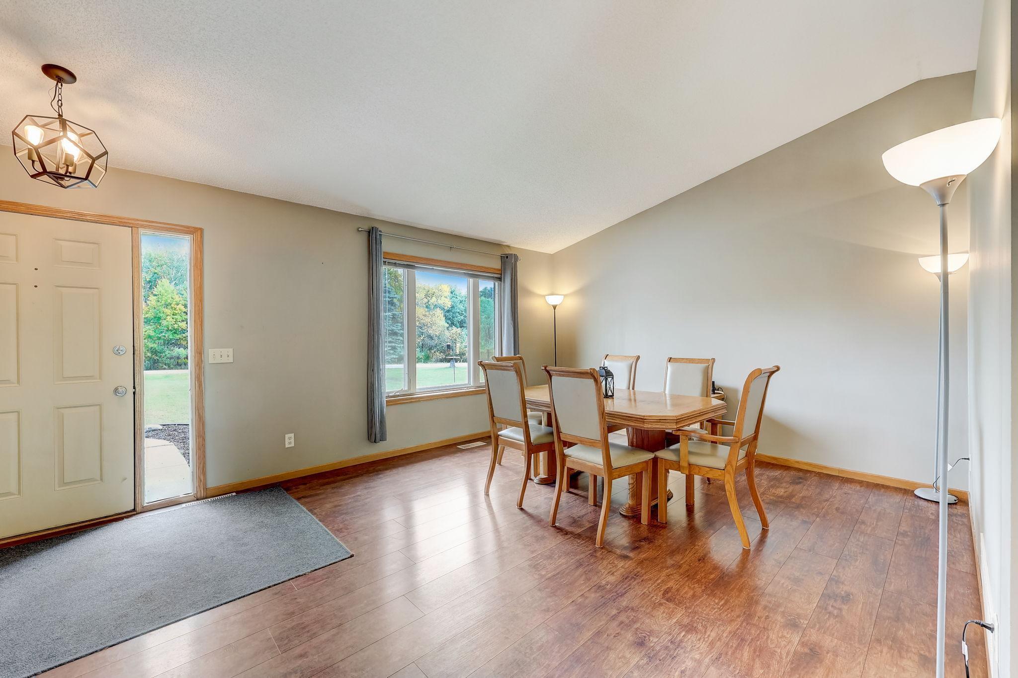 Dining area with a wooden table and chairs beside a large window and front entry.