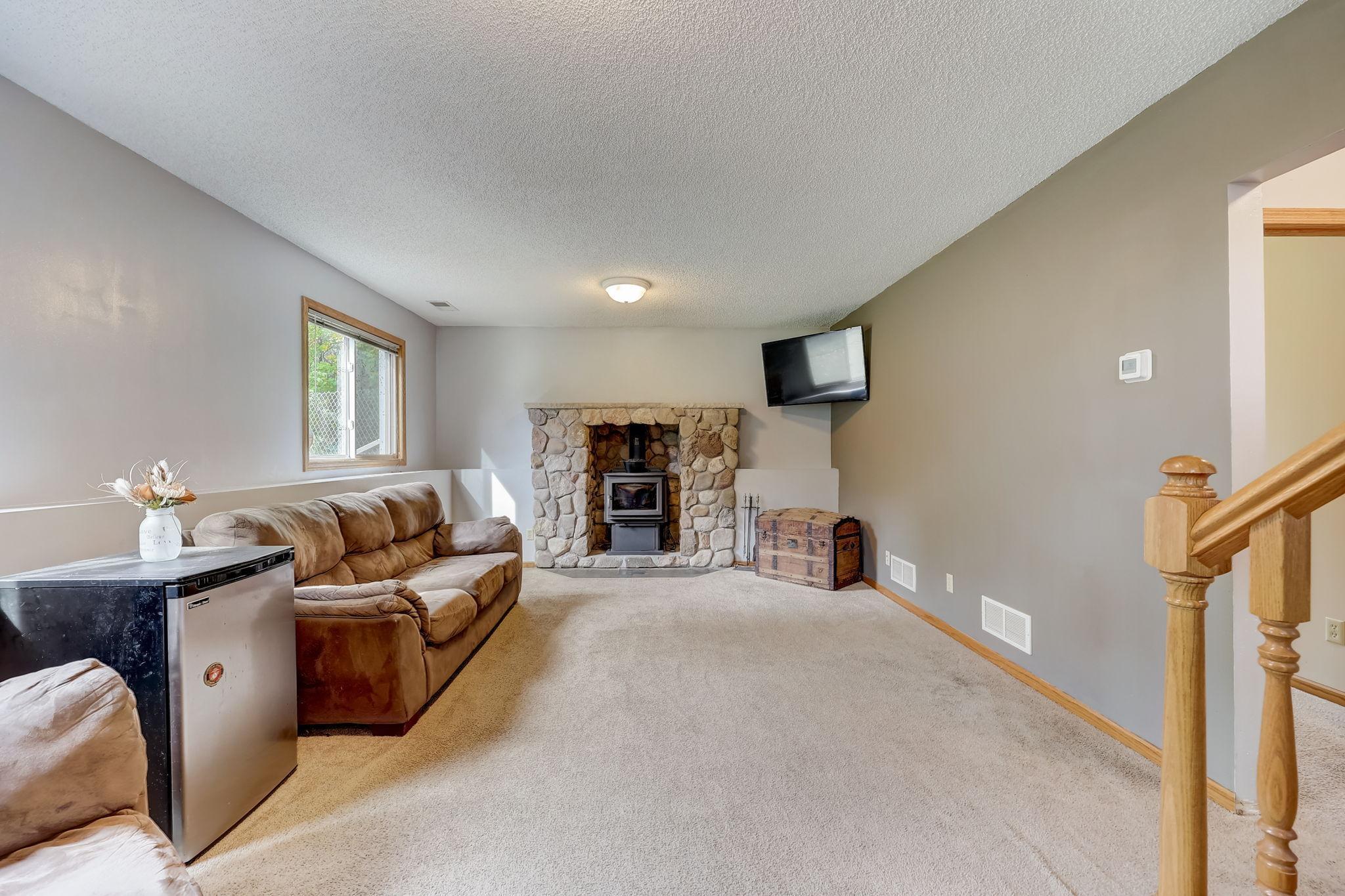 Living room with a stone fireplace, brown sofas, beige carpet, and wooden staircase railing.