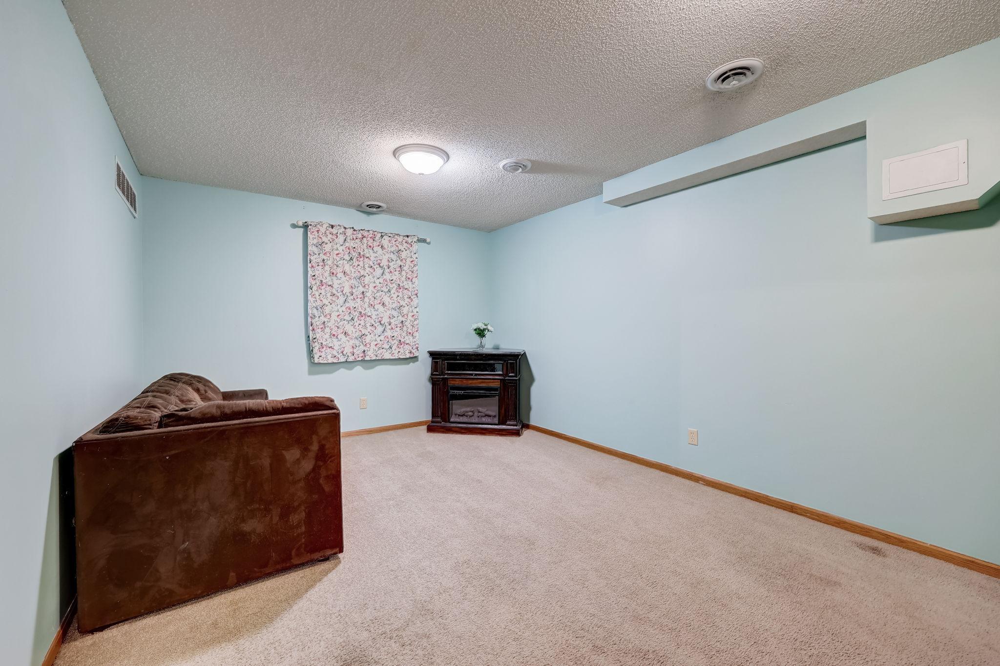 Living room with beige carpet, pale blue walls, a brown sofa, and a corner fireplace.