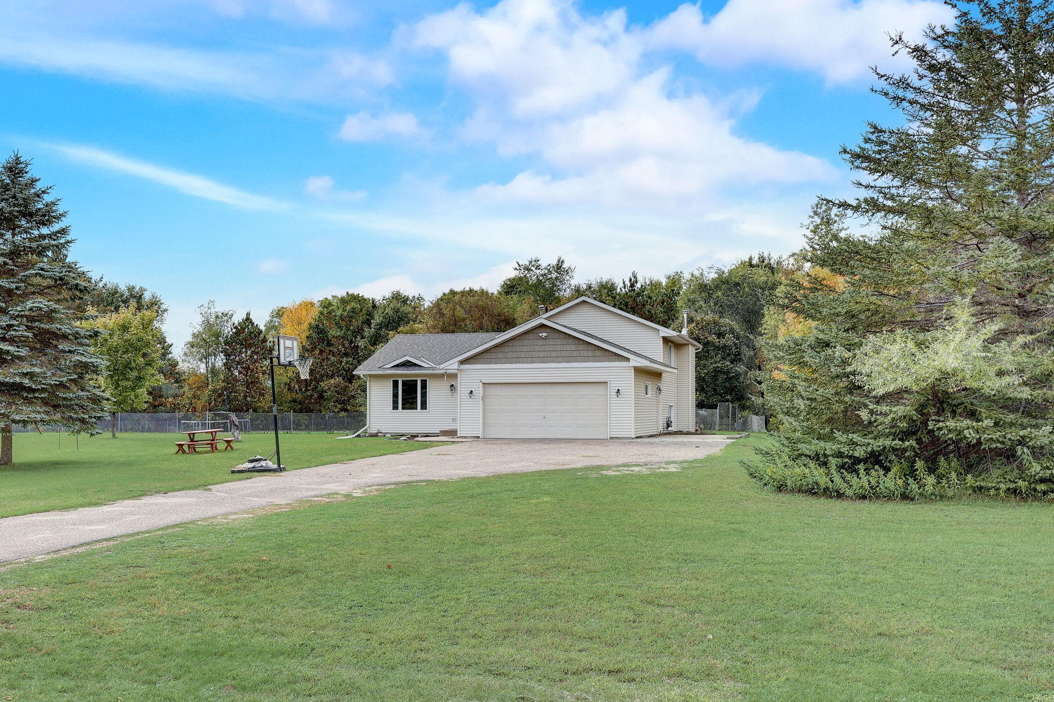 House with a two-car garage, broad lawn, basketball hoop, and picnic table.
