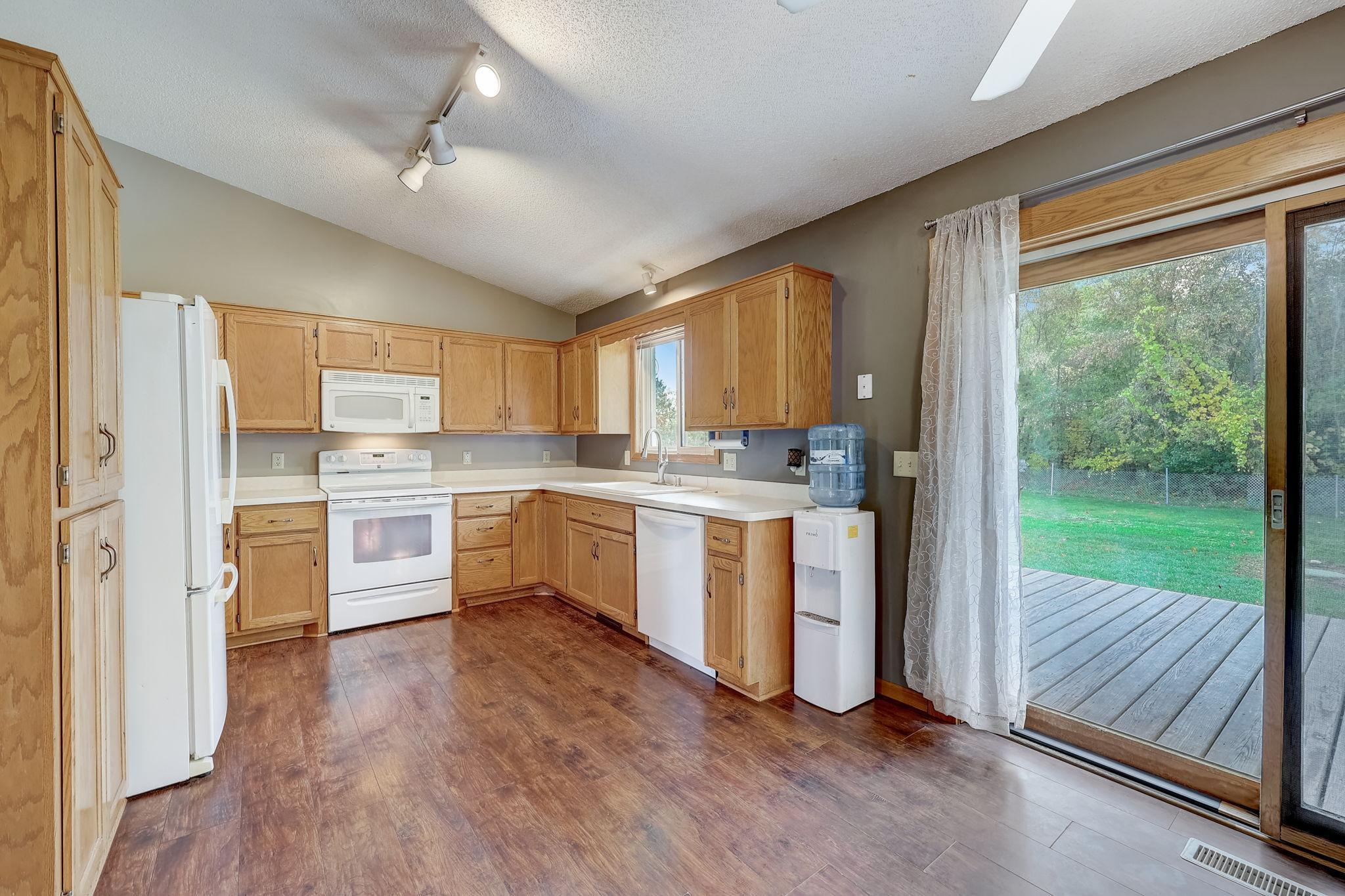 Kitchen with wood cabinets and white appliances, opening through a sliding glass door to a deck and yard.