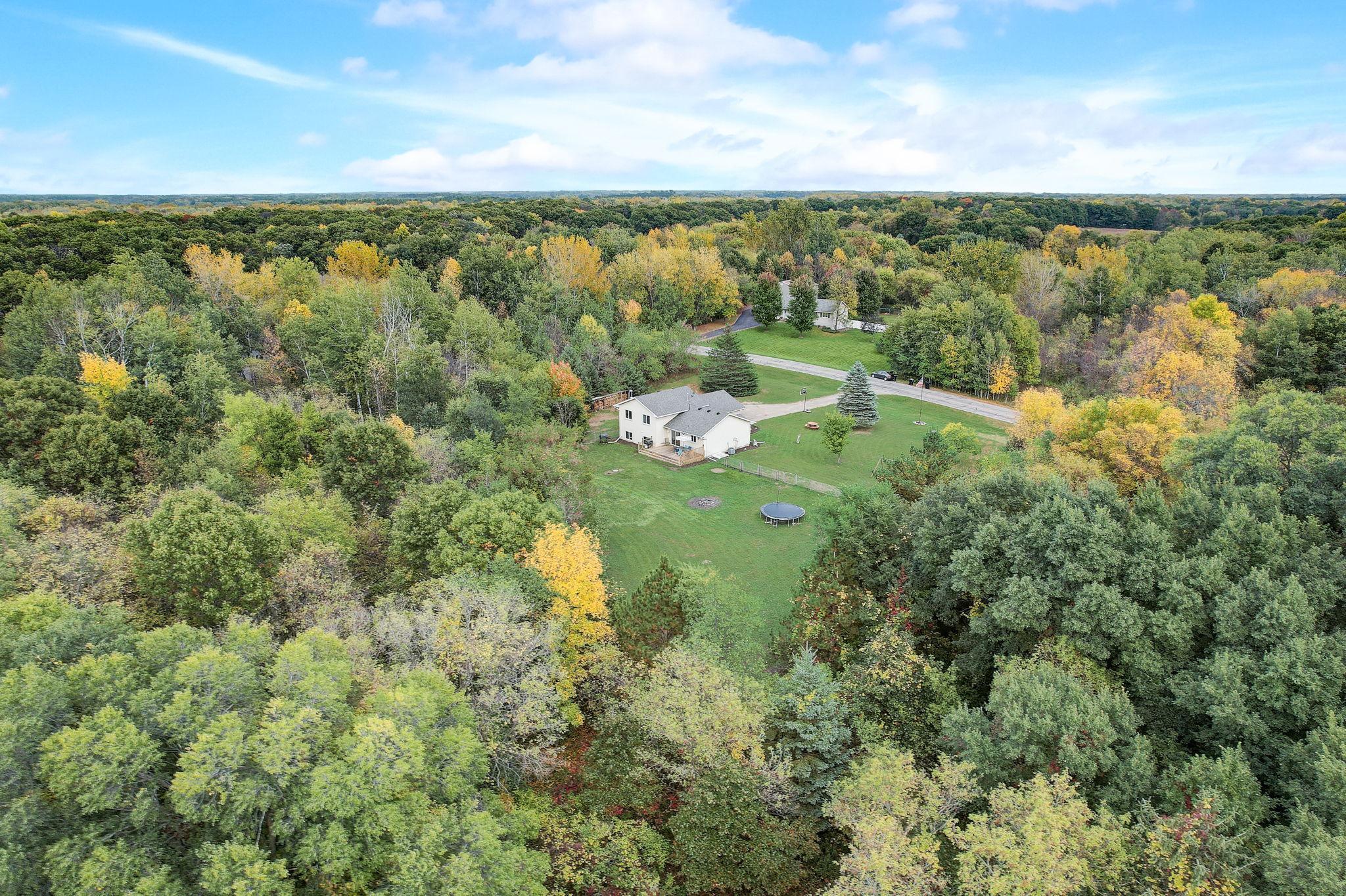 Aerial view of a home in a wooded clearing, with a large lawn and backyard trampoline.