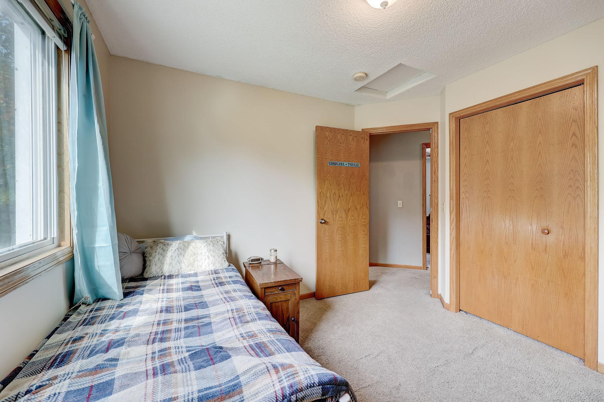 Bedroom with a plaid-covered bed, blue curtains, and an open wooden door bearing a small sign.