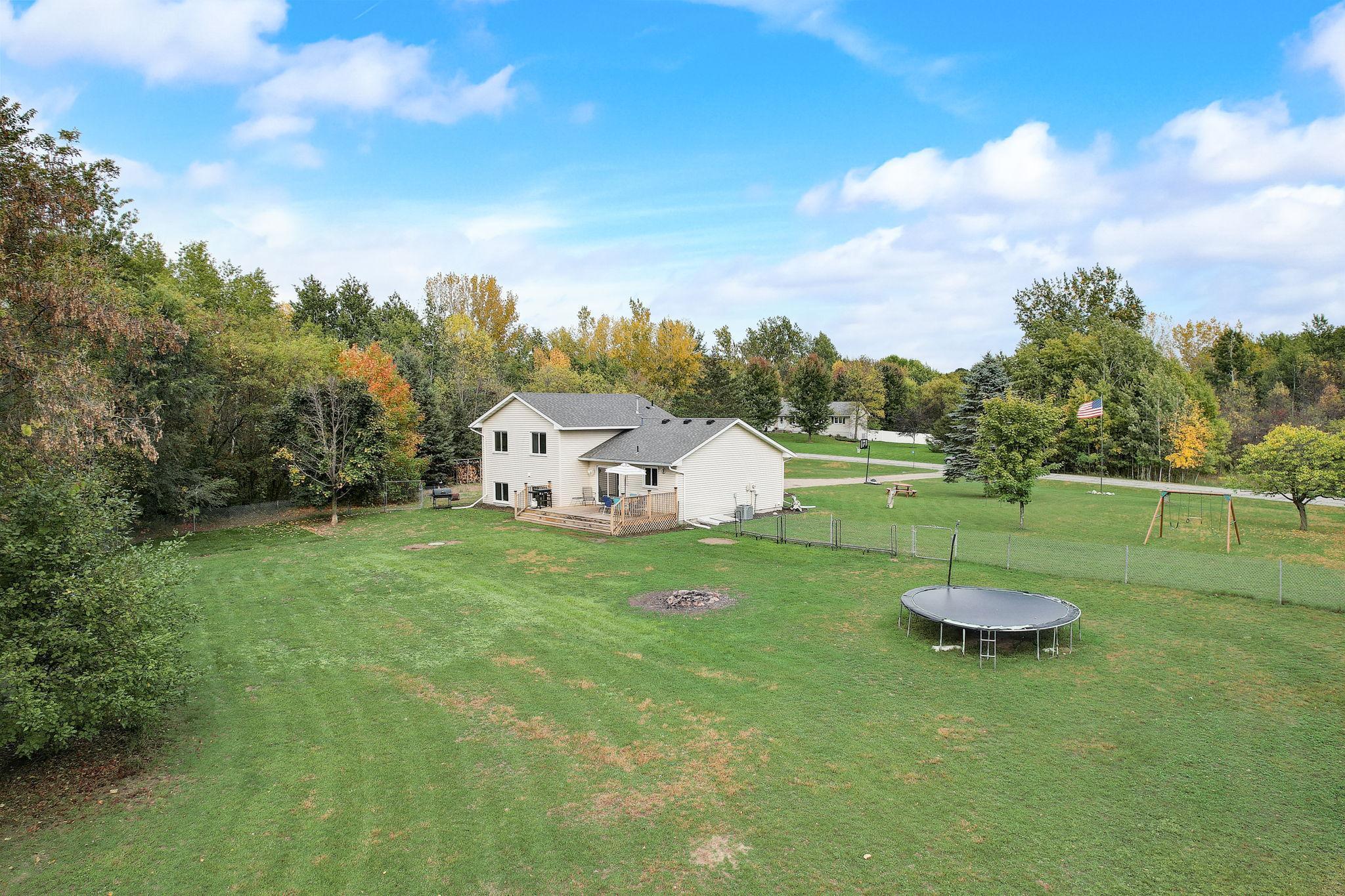 Aerial view of a two-story home with a spacious grassy backyard, trampoline, and autumn trees.