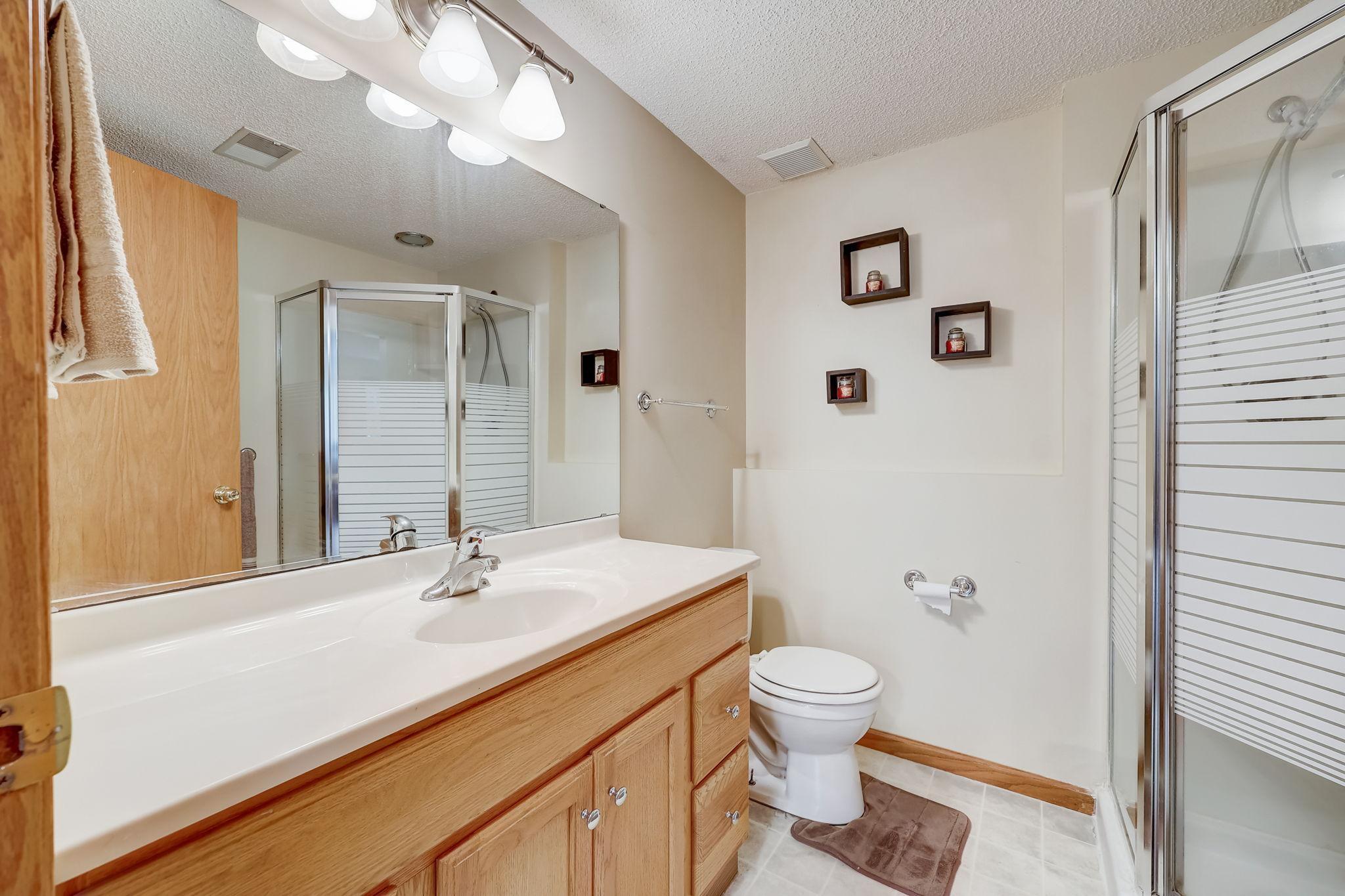 Bathroom with a wood vanity, large mirror, and glass-enclosed shower.
