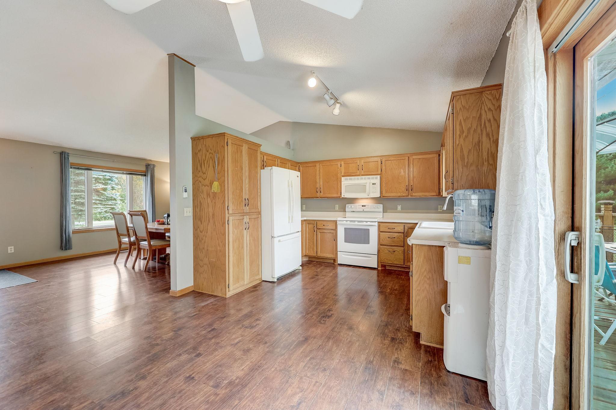 Kitchen with wood cabinets and white appliances, opening to a dining area and sliding glass door.
