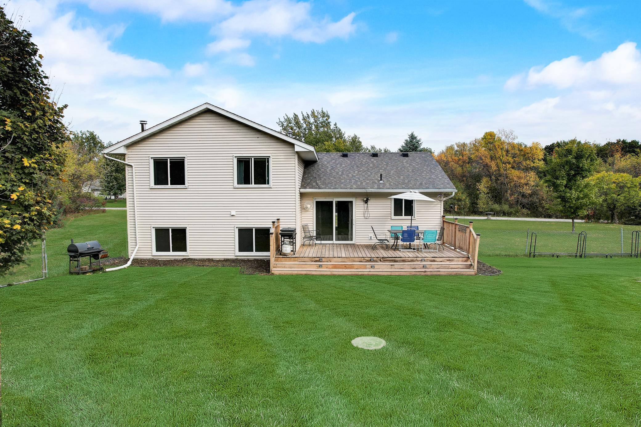 Rear of a two-story home with a wooden deck and spacious lawn bordered by trees.