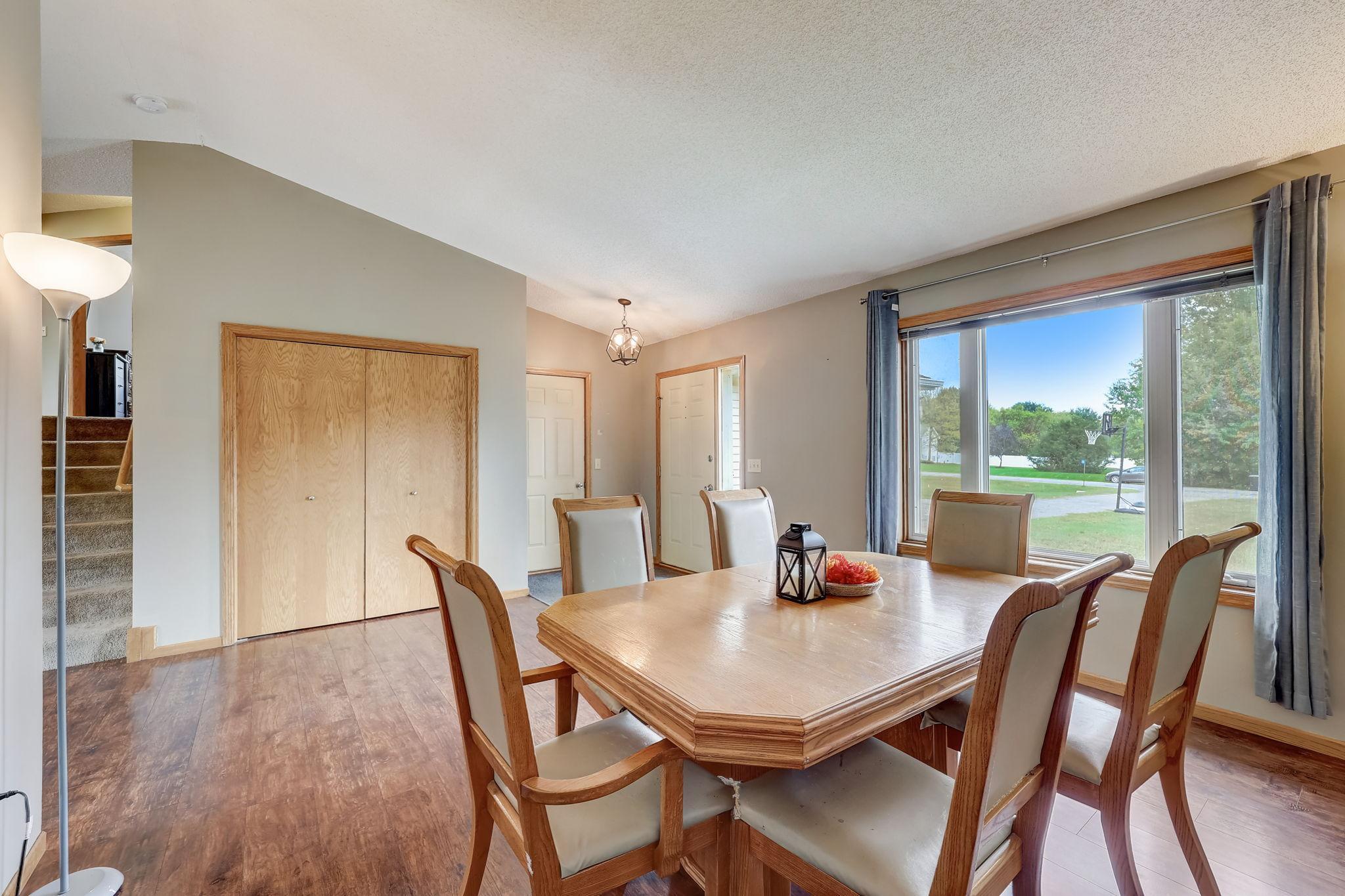 Dining room with a large wooden table beside a broad window and carpeted stairs.