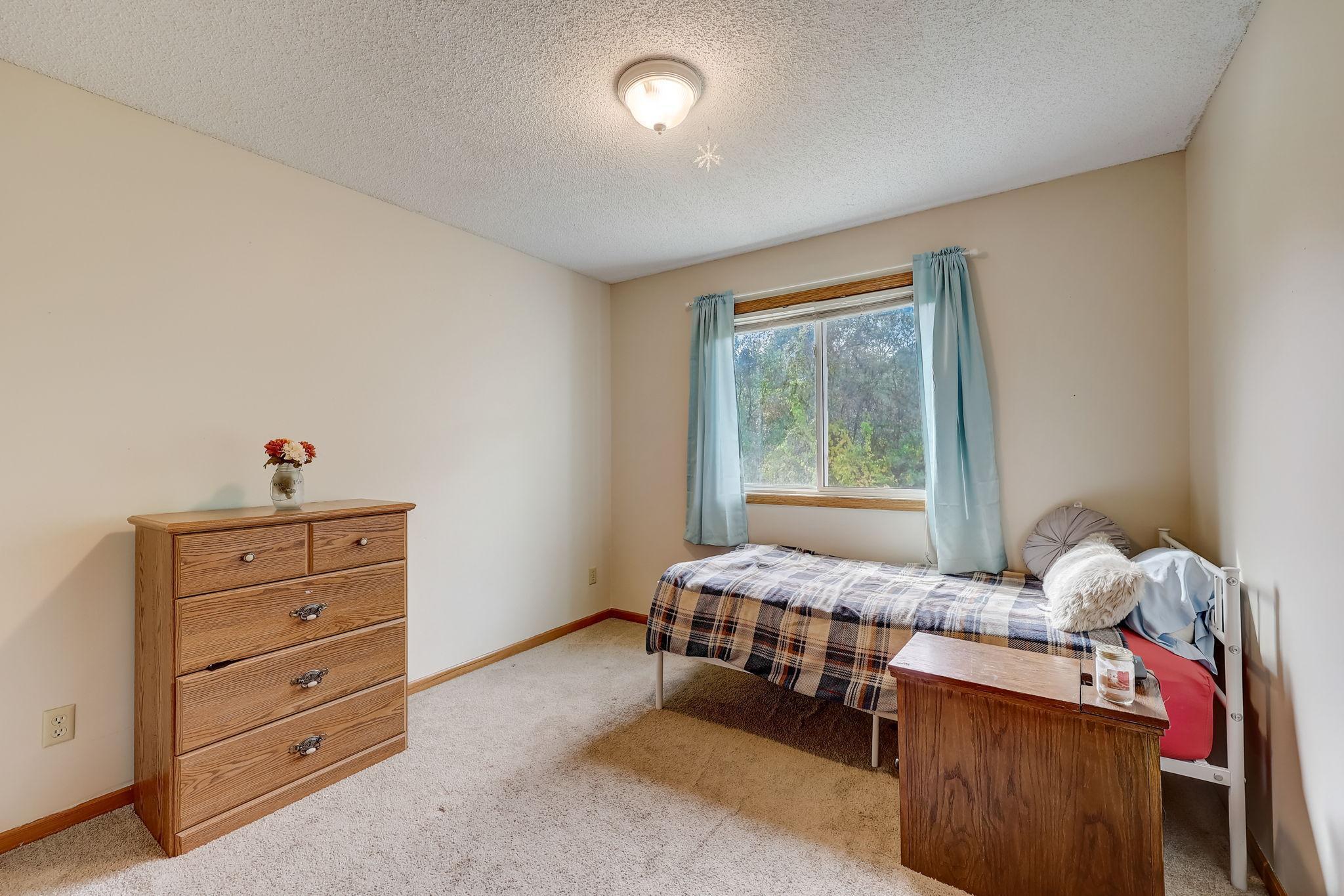 Bedroom with a single bed beneath a curtained window and a wooden dresser.
