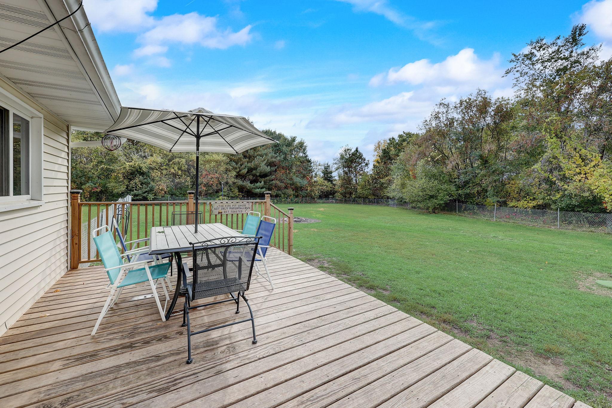 Wooden deck with an umbrella-shaded dining set overlooking a fenced grassy yard.
