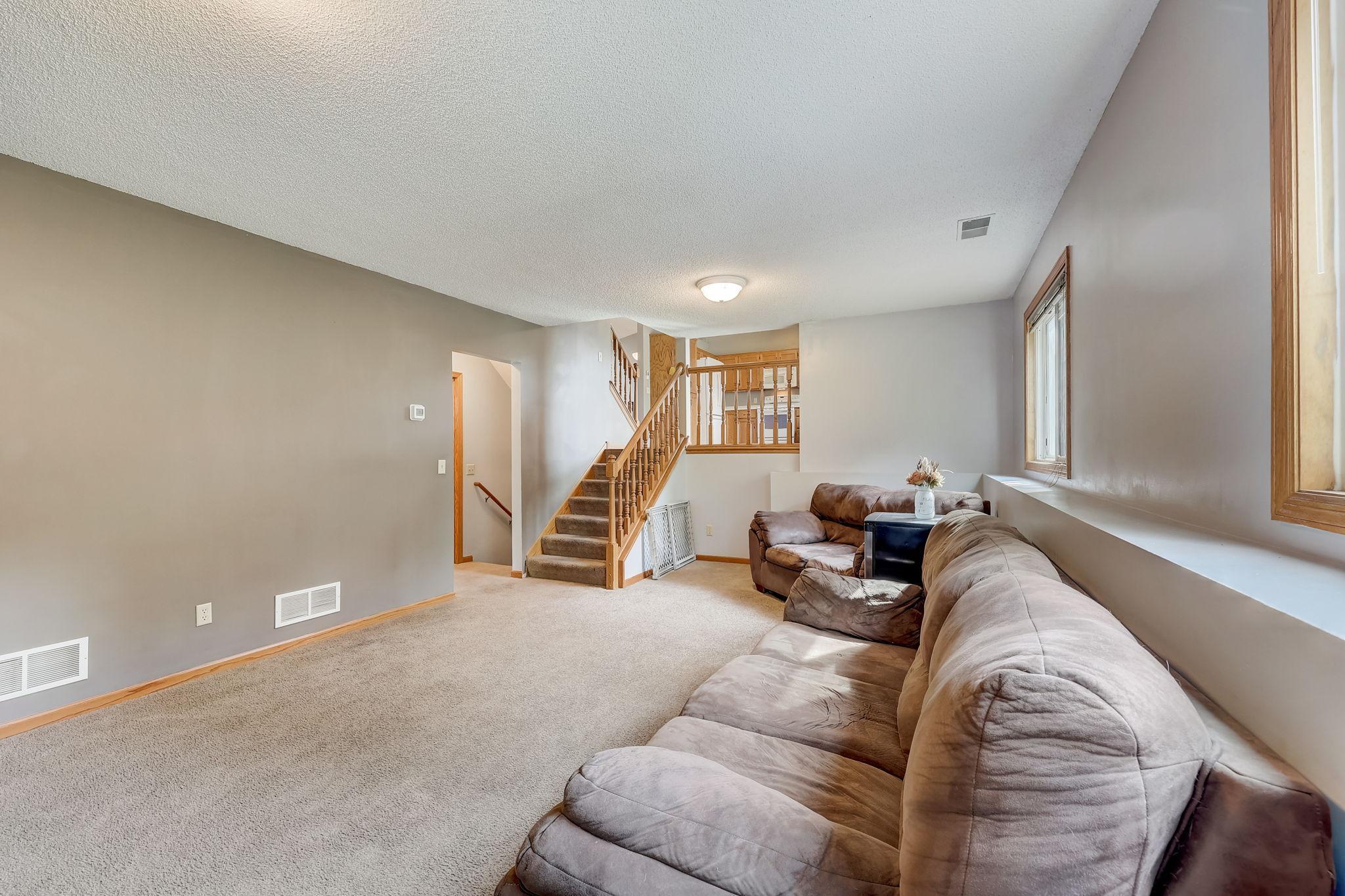 Living room with a brown sectional sofa, beige carpet, and a wood-railed staircase.