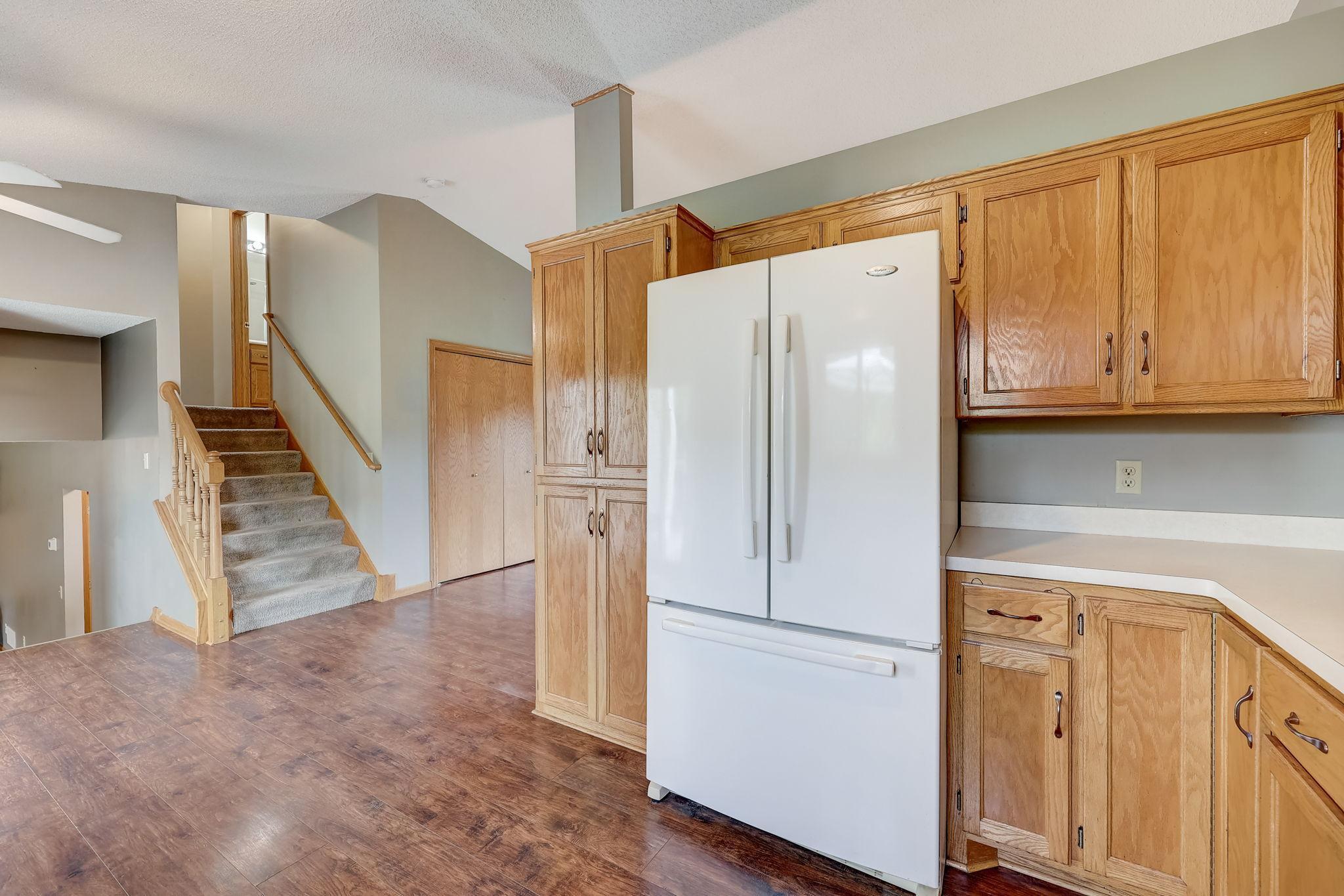 Kitchen with wood cabinets and white refrigerator beside a carpeted staircase.