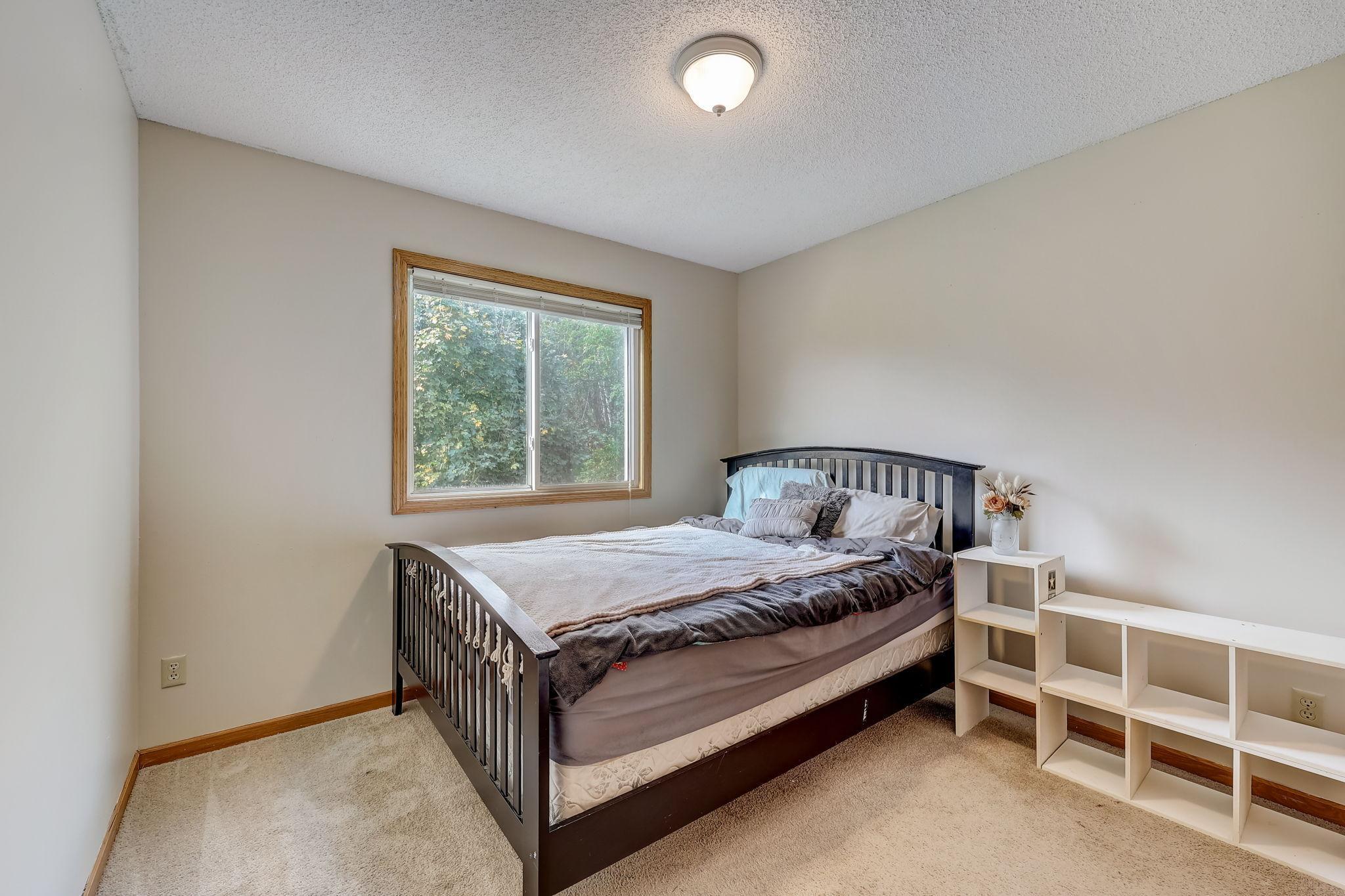 Bedroom with a dark wood bed, tree-facing window, beige carpet, and white open shelving.