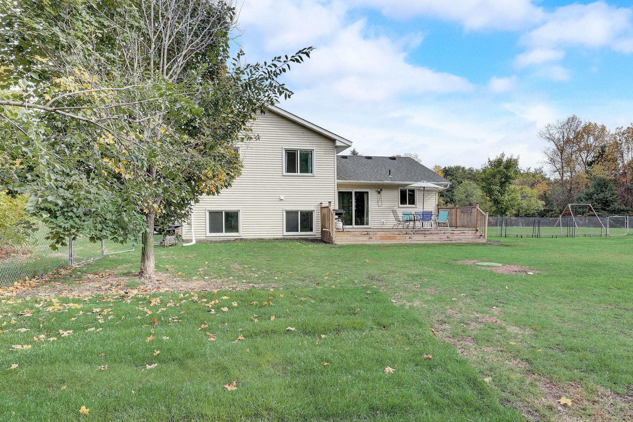 Rear of a two-story home with a wooden deck, fenced lawn, and swing set.