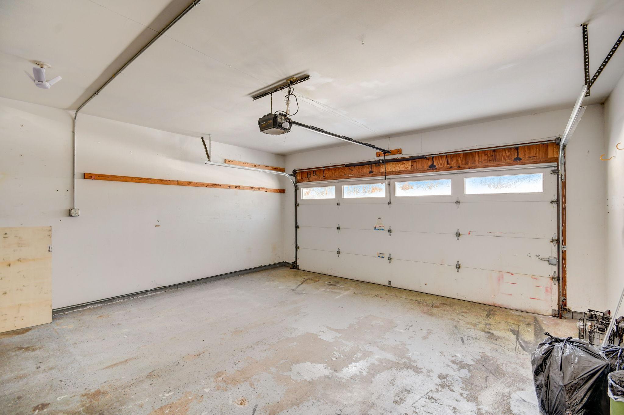 Empty garage with a concrete floor, overhead door, and a few bags in one corner.