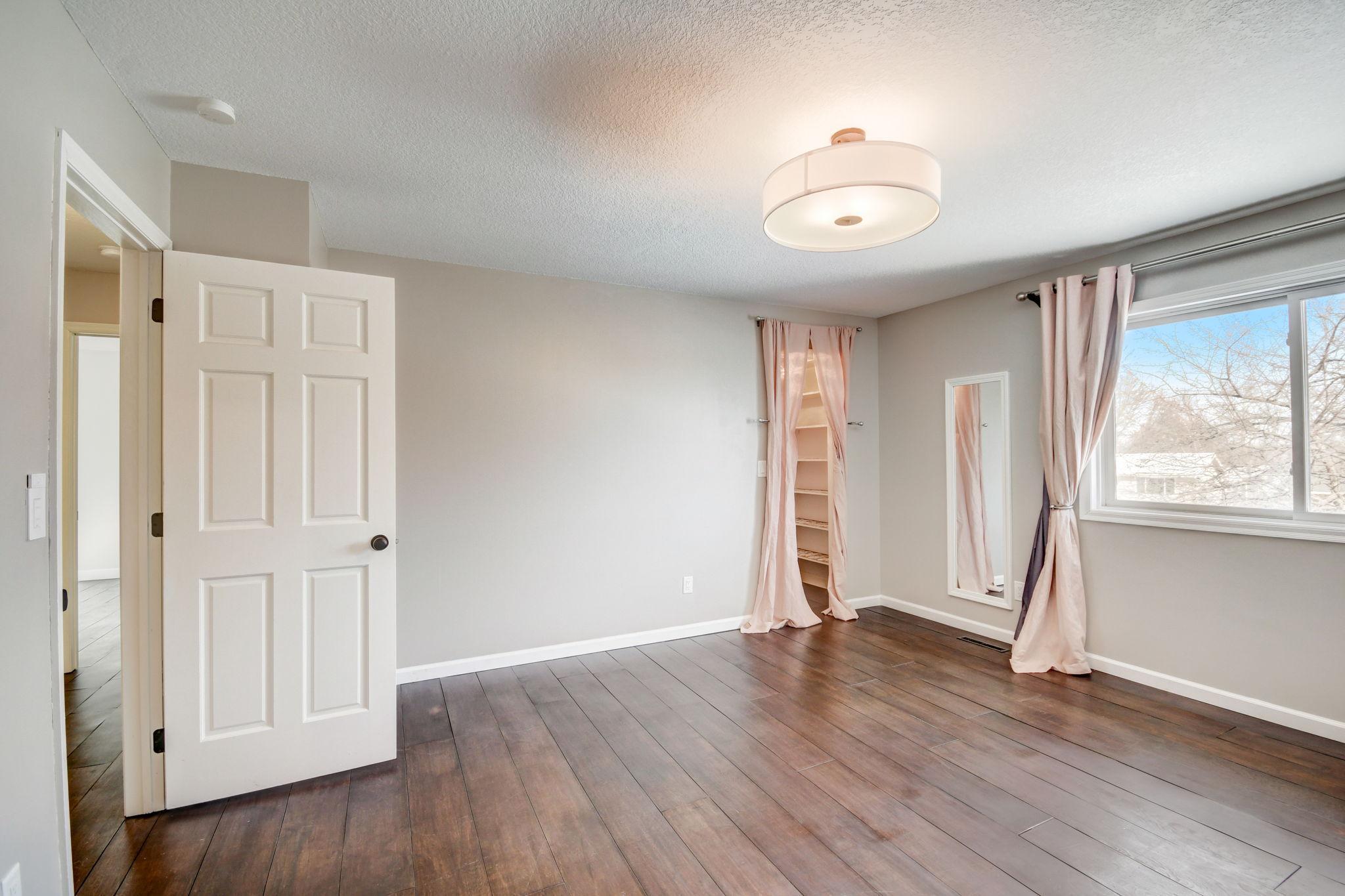 Empty bedroom with dark flooring, a curtained shelving nook, and a large window.