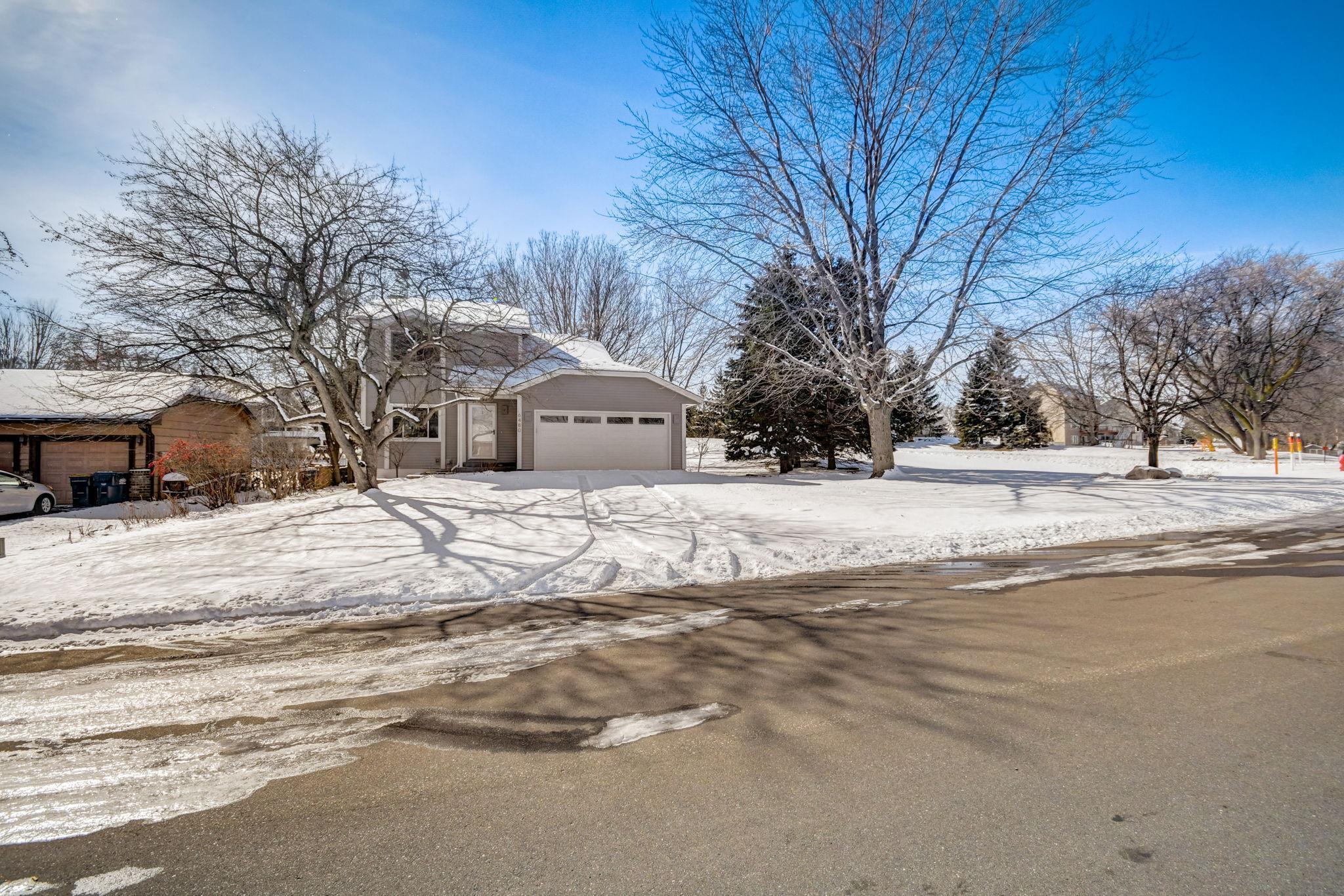 Gray split-level house with two-car garage behind a snow-covered yard and bare trees.