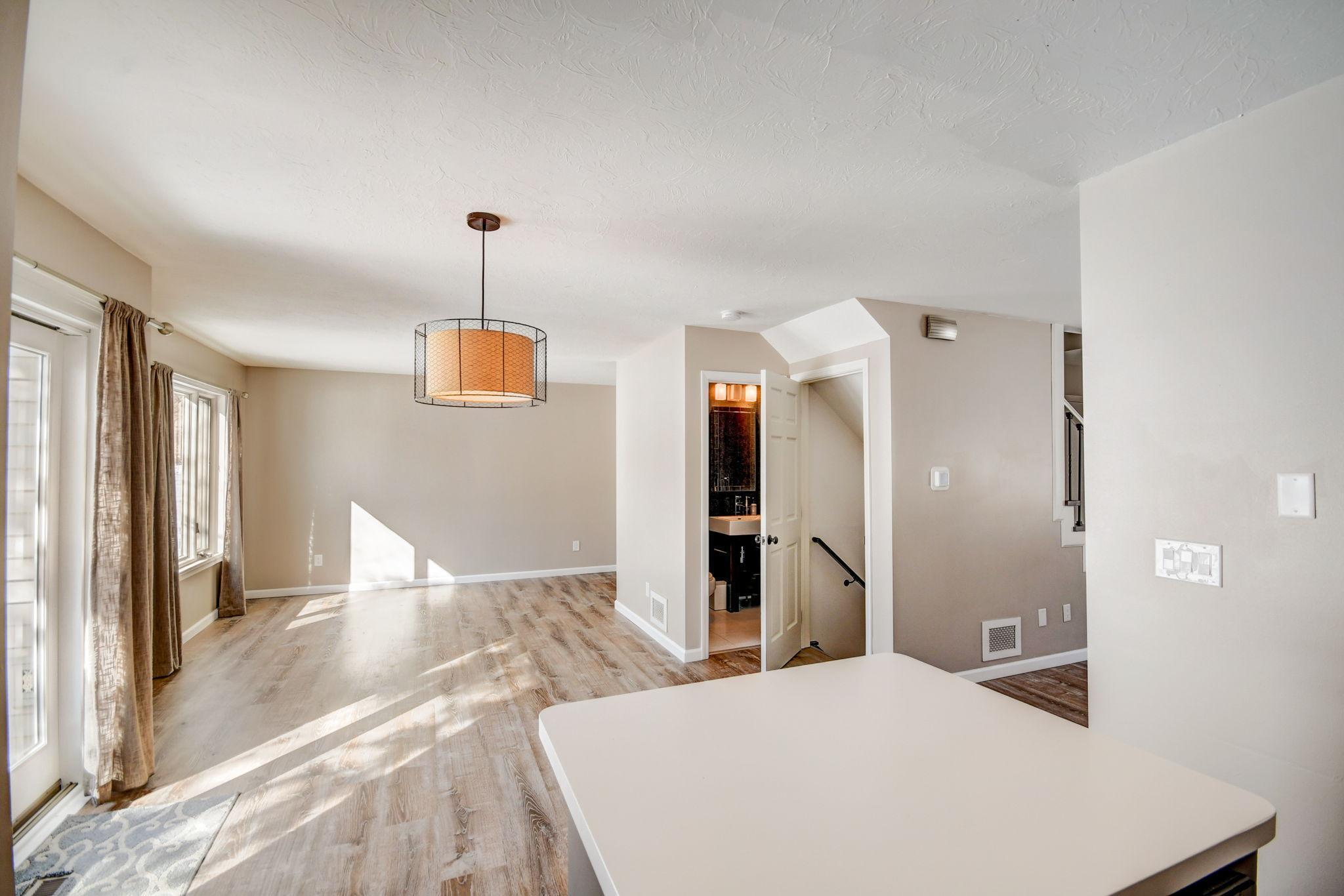 Vacant kitchen and dining area with a white island, wood-look floors, and sunlight through tall windows.