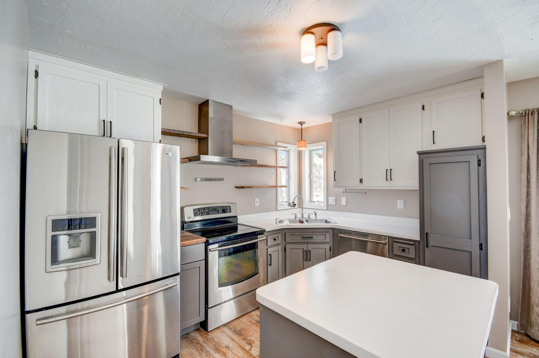 Kitchen with stainless steel appliances, gray lower cabinets, corner sink, and a large white island.