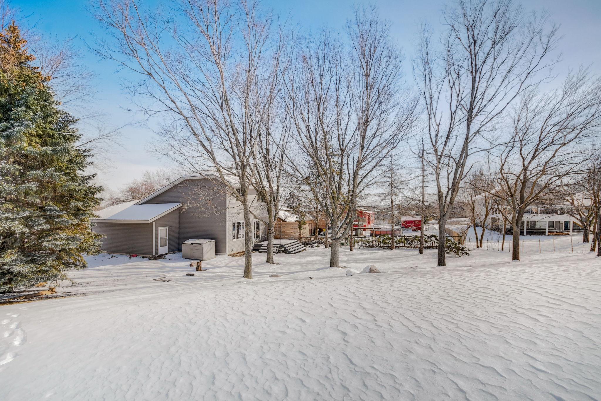 Gray house behind a snow-covered yard, framed by bare trees and an evergreen.