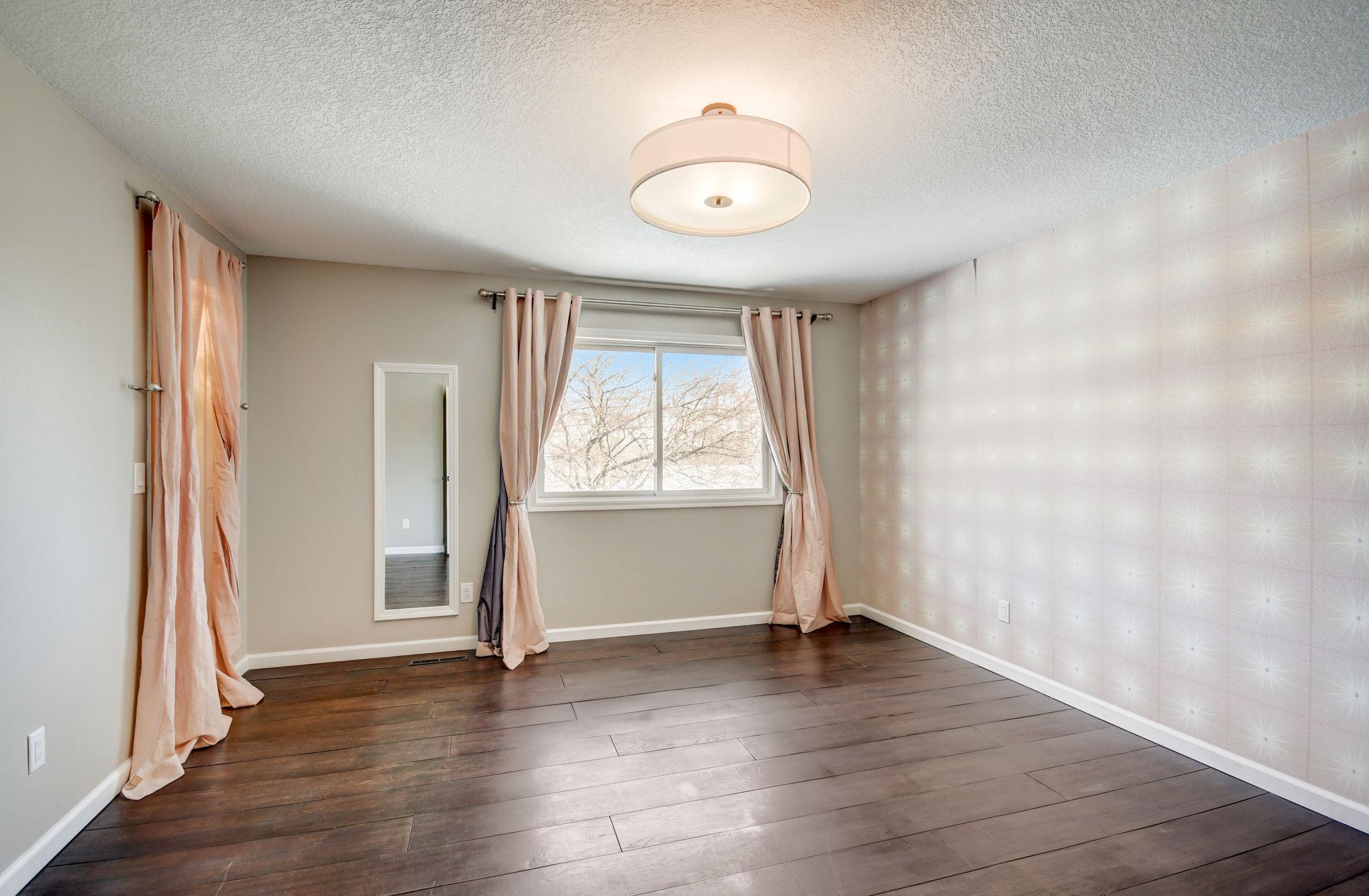 Unfurnished bedroom with dark wood floors, a patterned accent wall, and a curtained window.