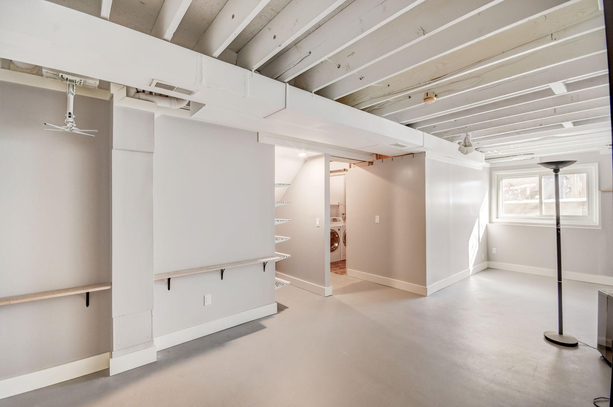 Basement room with exposed ceiling beams, built-in shelves, and a laundry area.